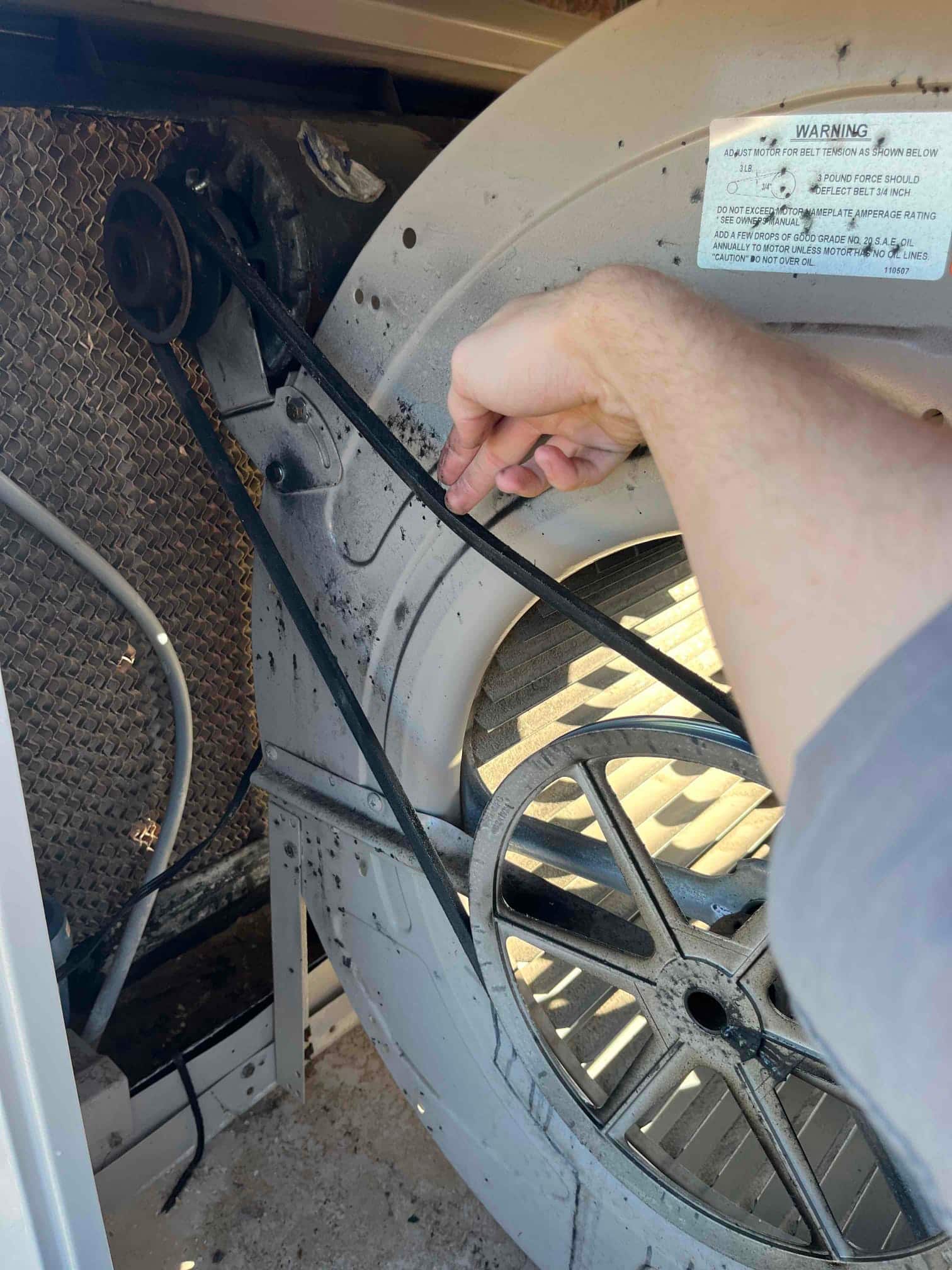 Technician hand installs a new drive belt on a large blower pulley inside an HVAC air handler cabinet.