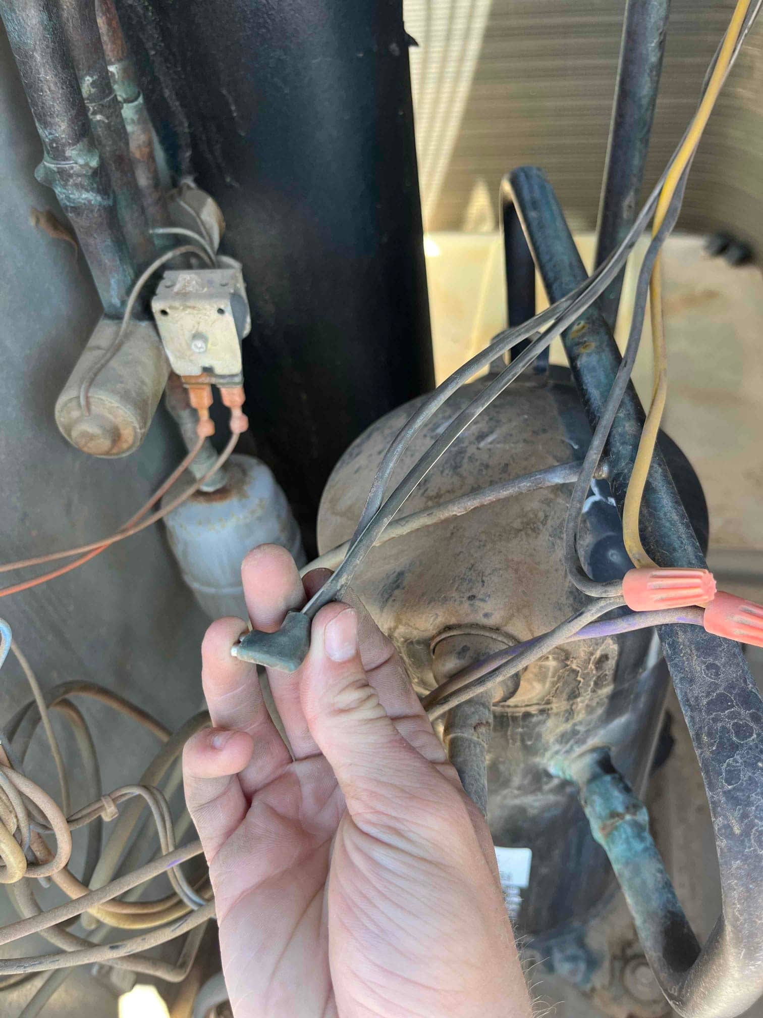 Technician holds disconnected compressor wires near wire nuts and terminals inside the condenser, adjacent to the compressor and contactor.