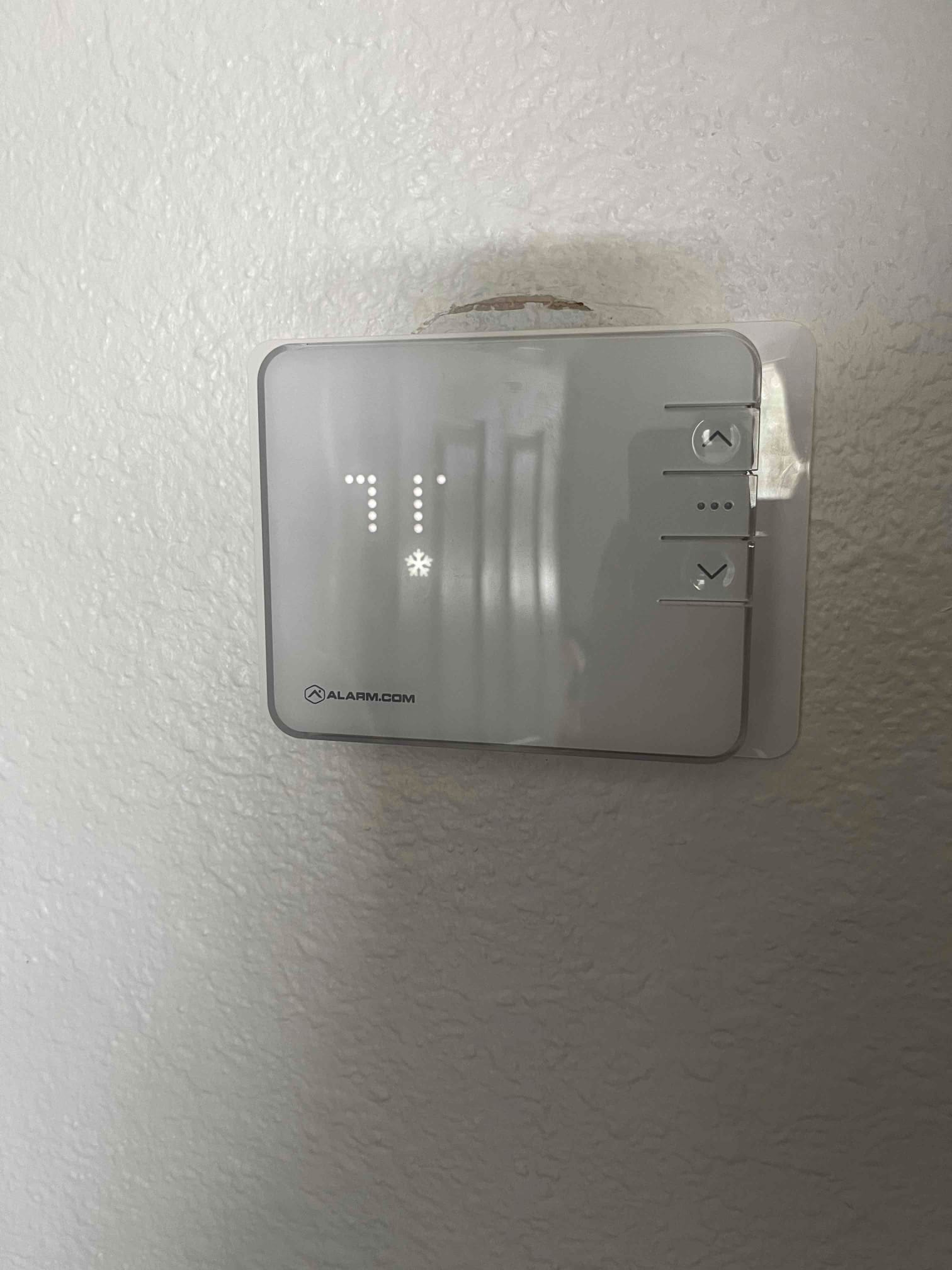 Wall-mounted thermostat displays a cooling setpoint with illuminated snowflake icon and touch controls on the right side.
