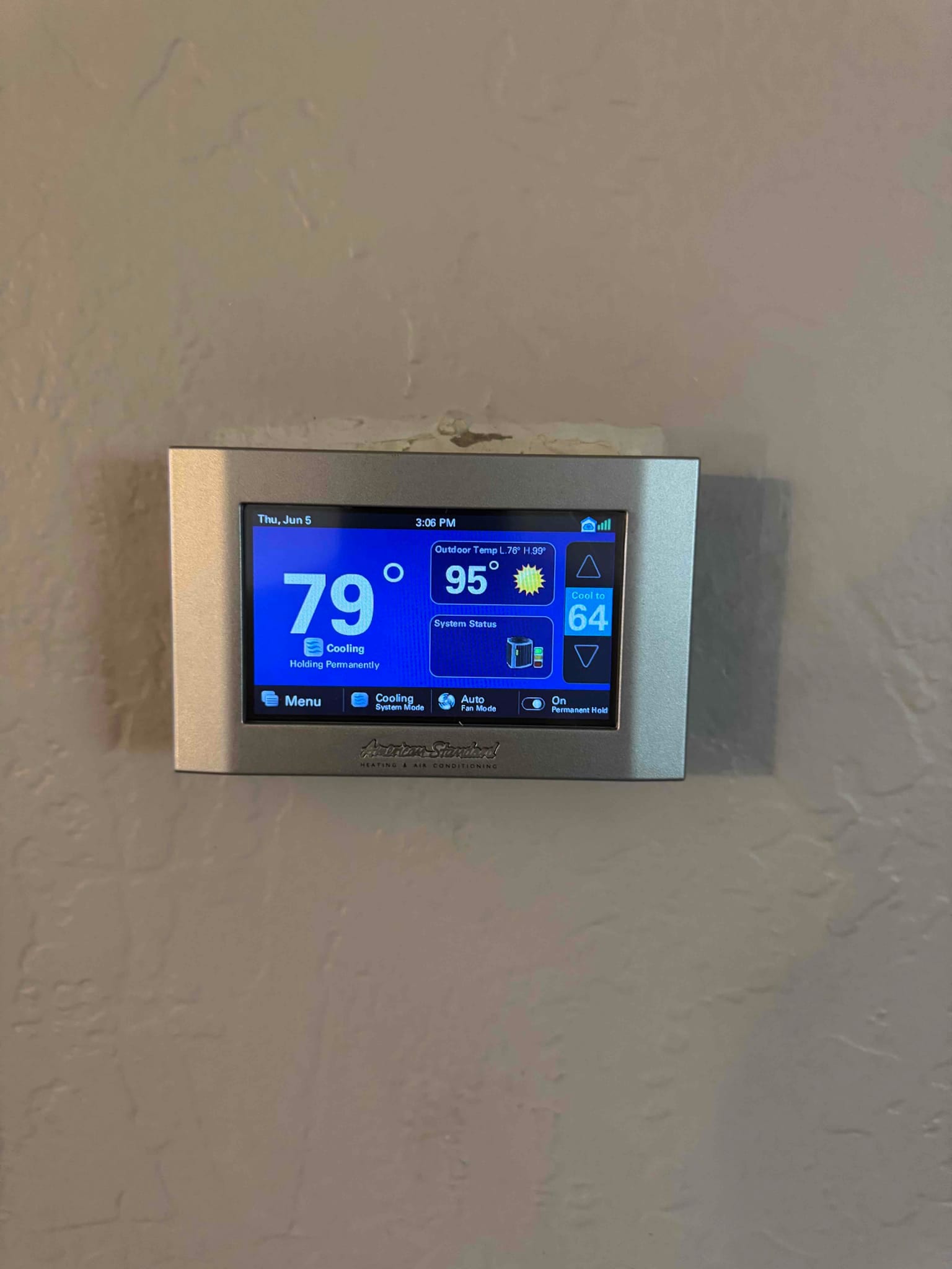 Wall-mounted touchscreen thermostat displays indoor temperature and active cooling mode after system installation.