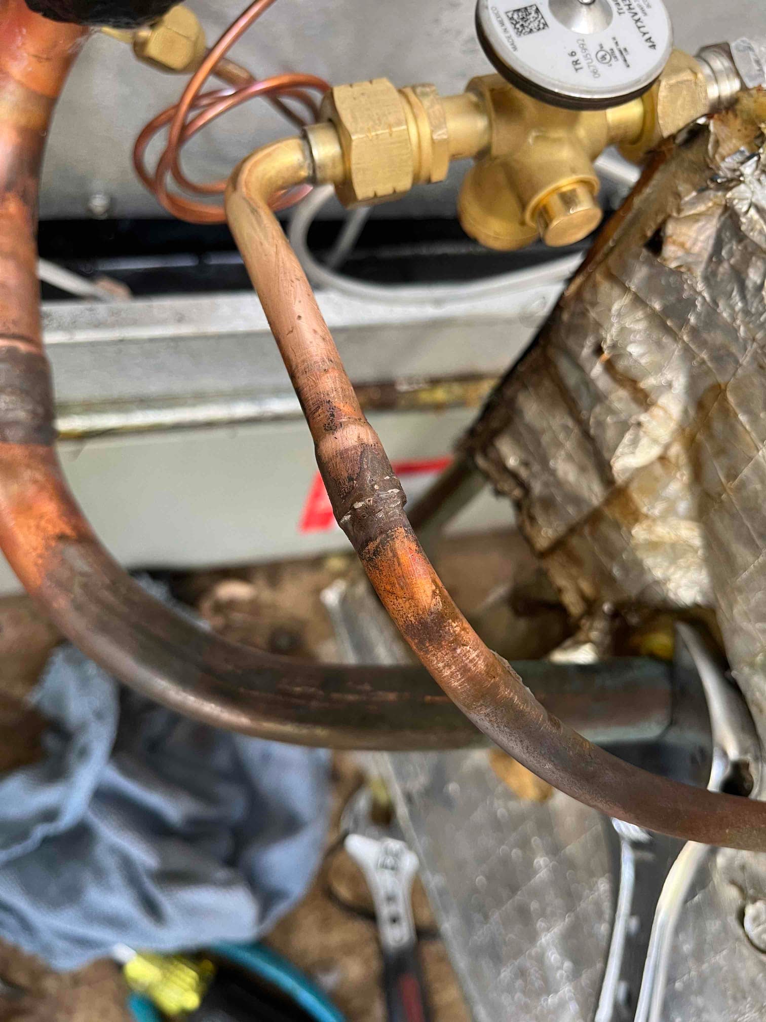 Brazed copper refrigerant lines near a TXV fitting, showing heat discoloration and surrounding insulation and tools at the air handler.