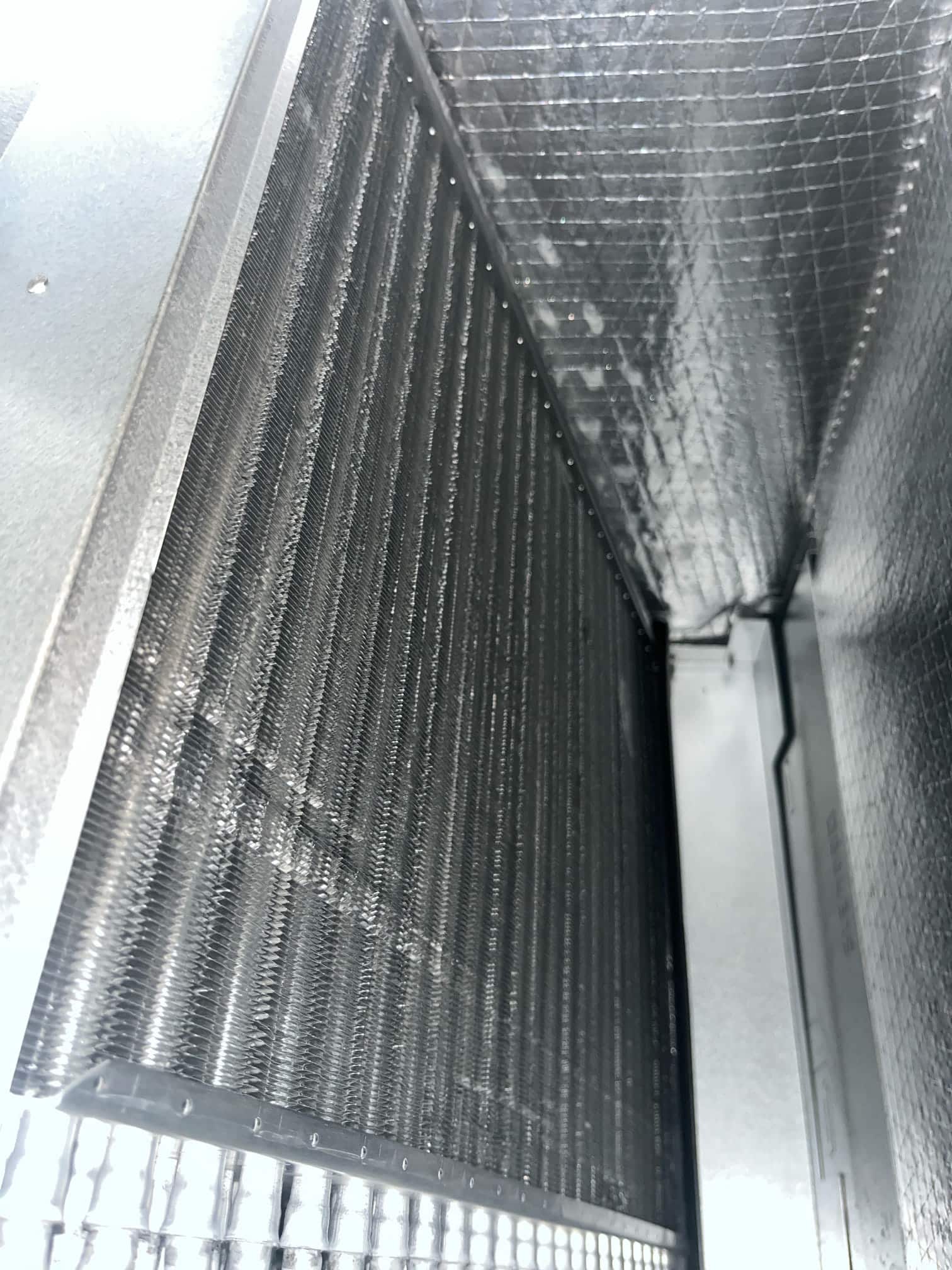 Clean evaporator coil fins inside an insulated air handler cabinet after replacement, with bright reflective foil-faced insulation lining the plenum.