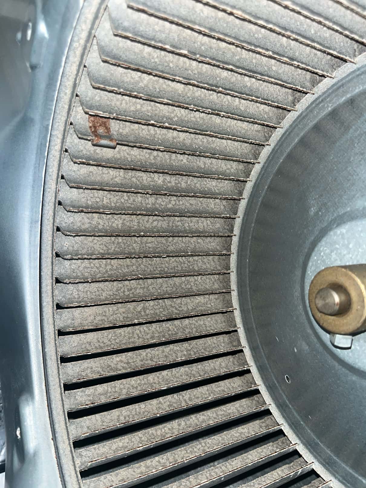 Close-up of a dusty blower wheel and housing inside an HVAC air handler, showing accumulated debris on the fins.