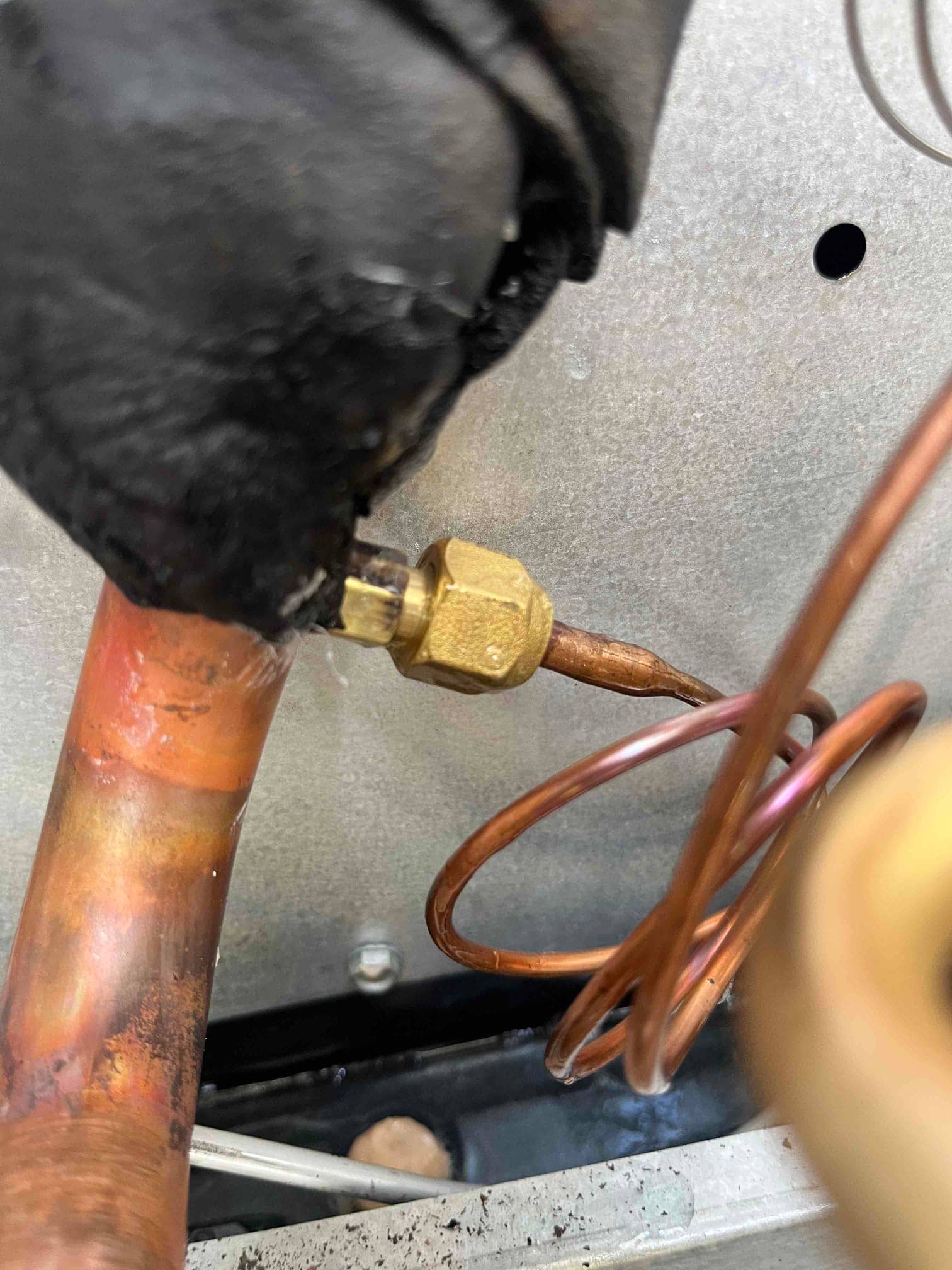 Close-up of a thermal expansion valve sensing bulb secured to a copper suction line with insulation partially removed.