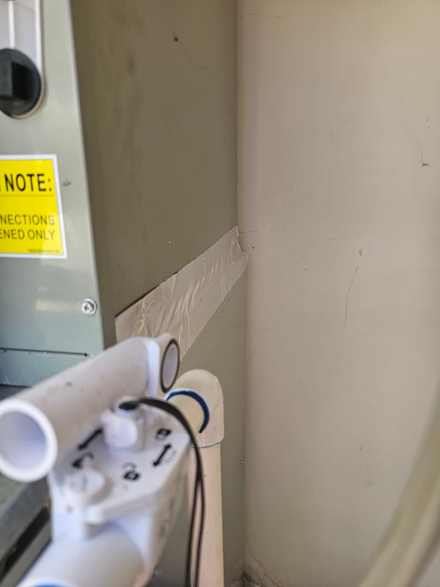 Condensate drain assembly with cleanout and float switch installed beside the air handler, wall penetration sealed with tape.