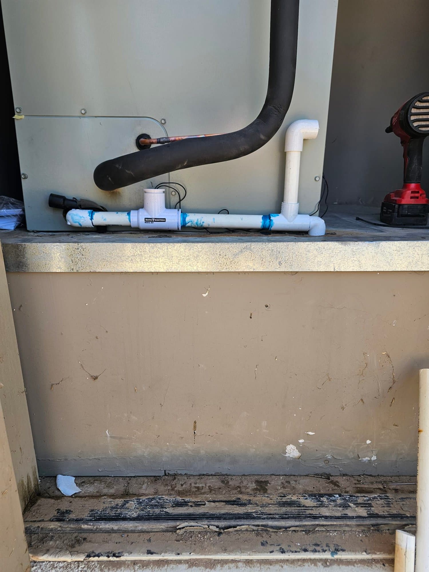 Condensate drain assembly with cleanout and trap installed beneath the air handler, alongside insulated suction line and service tools.