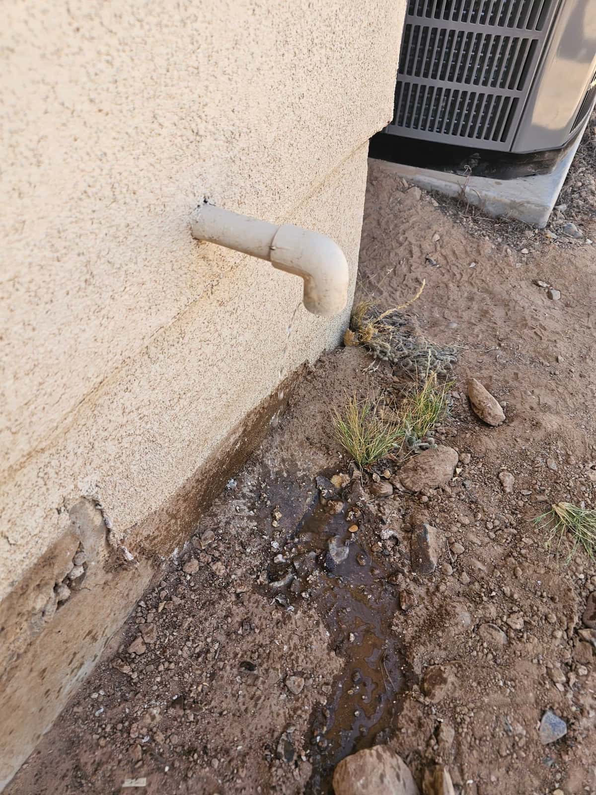 Condensate drain line terminates outside, discharging water near the new outdoor unit on a level pad.