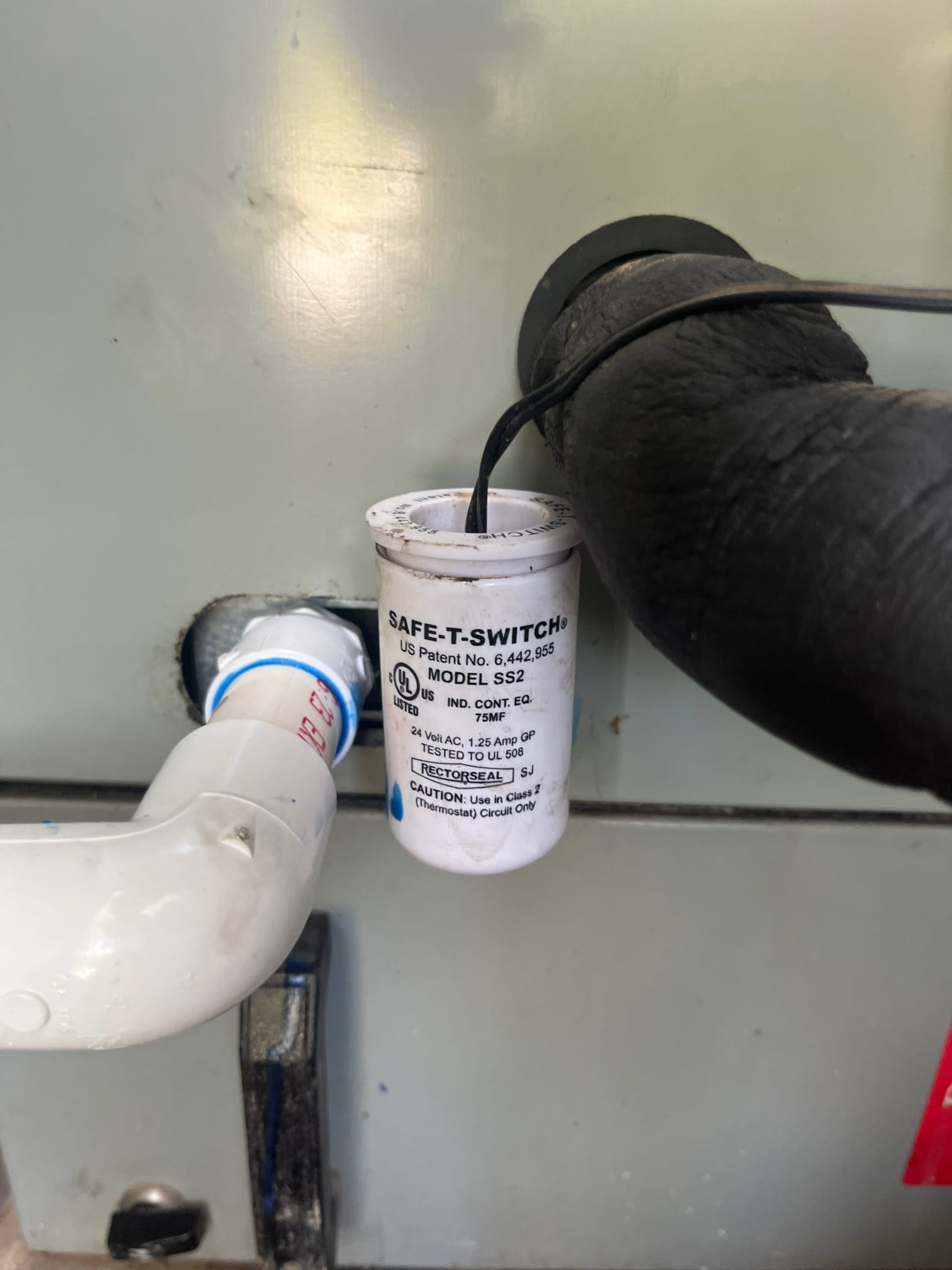 Condensate float safety switch installed on the drain line with insulated suction line and PVC piping at the air handler.