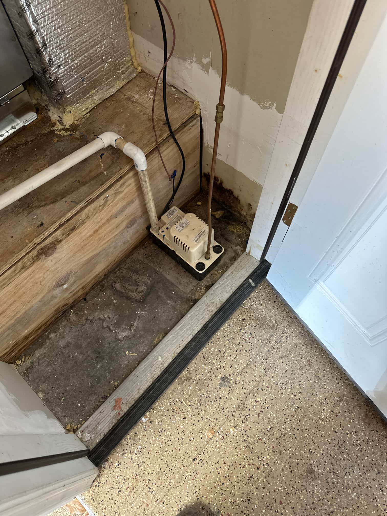 Condensate pump installed beside the air handler platform with PVC drain connection and nearby copper refrigerant line.
