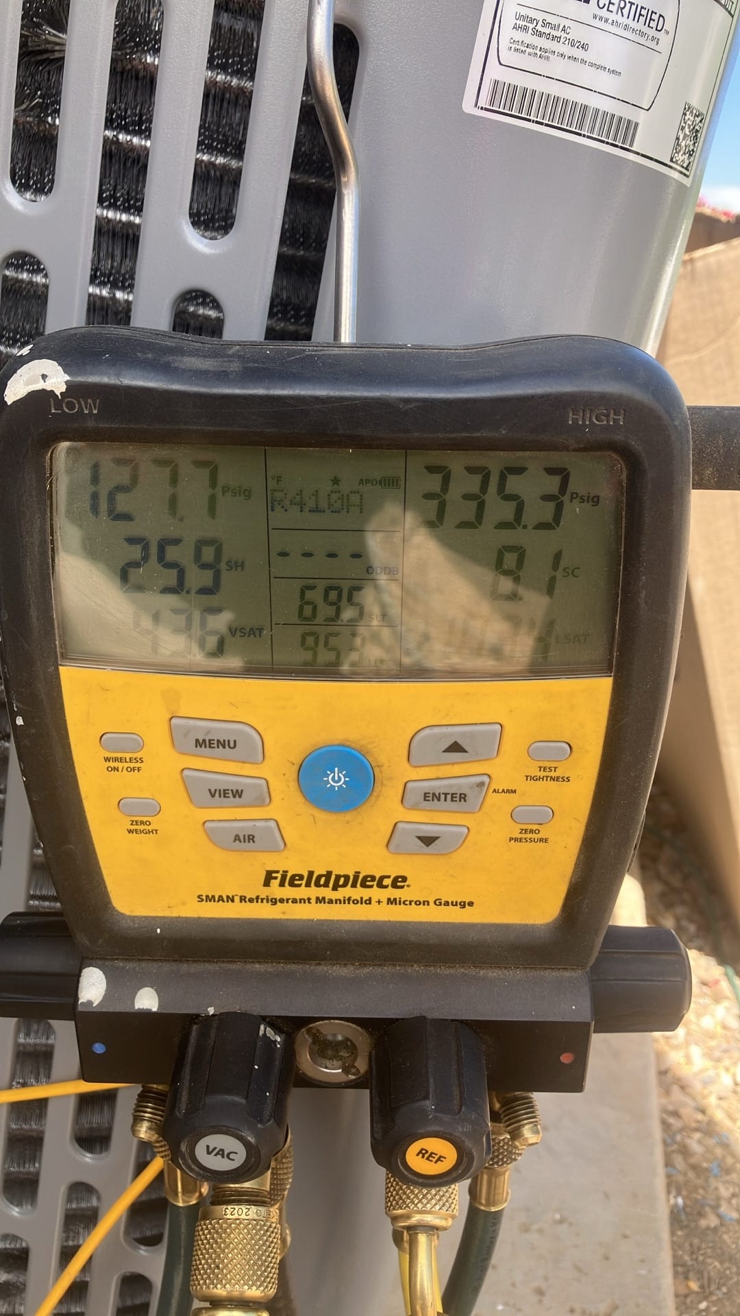 Digital manifold connected to the outdoor unit shows 127.7 PSI suction and 335.3 PSI liquid during system operation with R-410A.