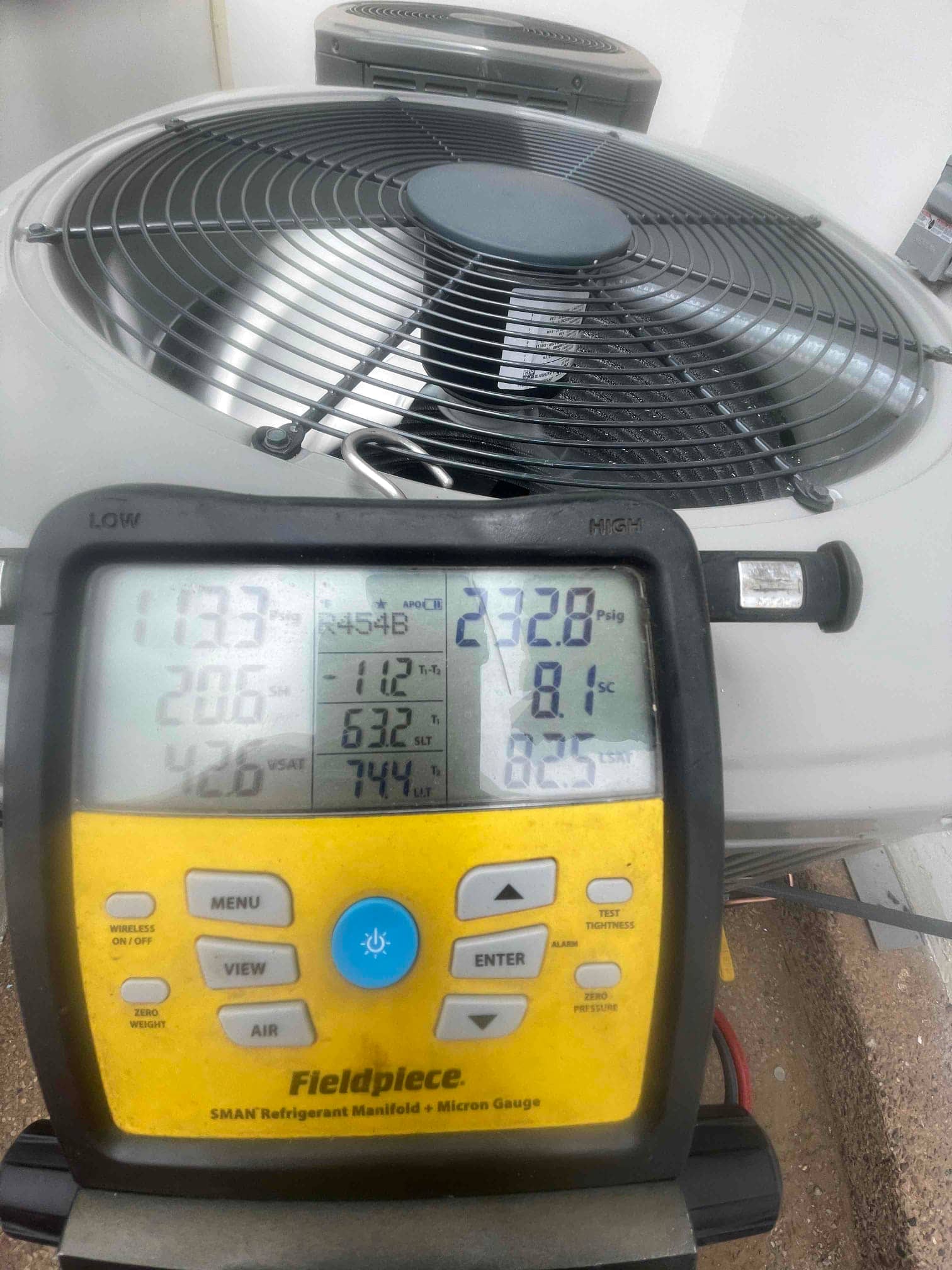 Digital manifold connected at the outdoor unit shows operating pressures and refrigerant type during system commissioning.