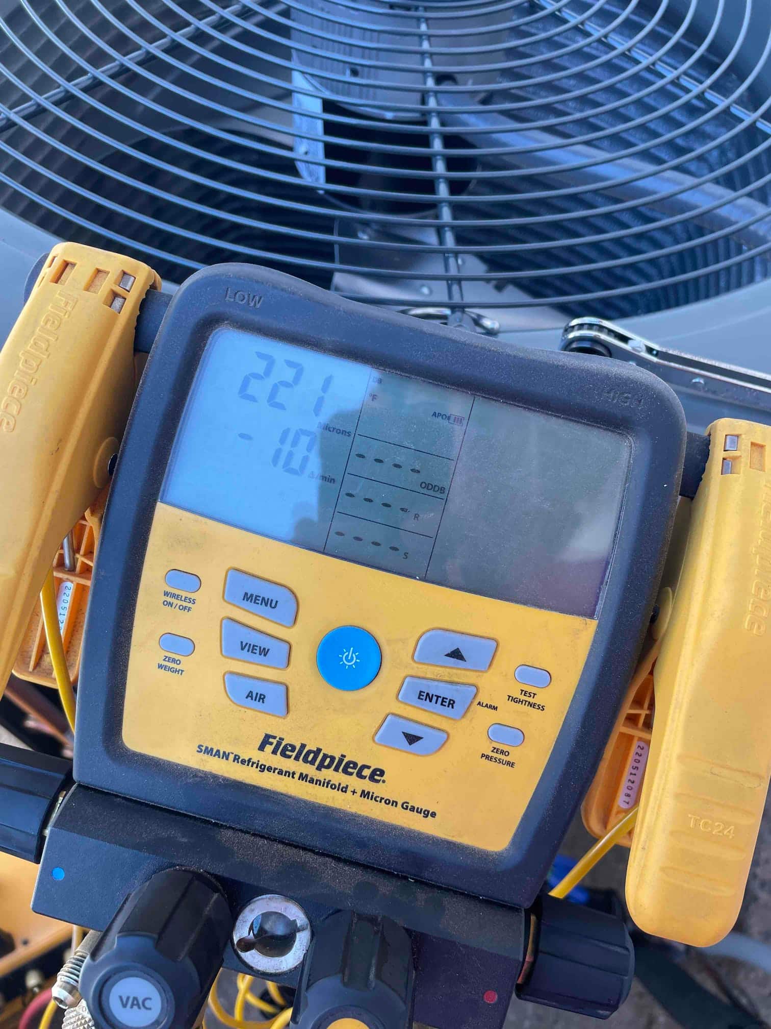 Digital micron gauge on the condenser shows 221 microns, confirming deep vacuum during system evacuation before refrigerant charging.