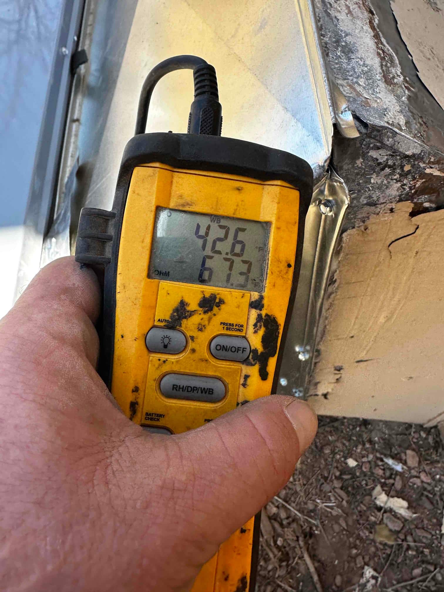 Digital thermometer displays 42.6°F and 67.3°F while checking air temperatures during commissioning at the duct connection.