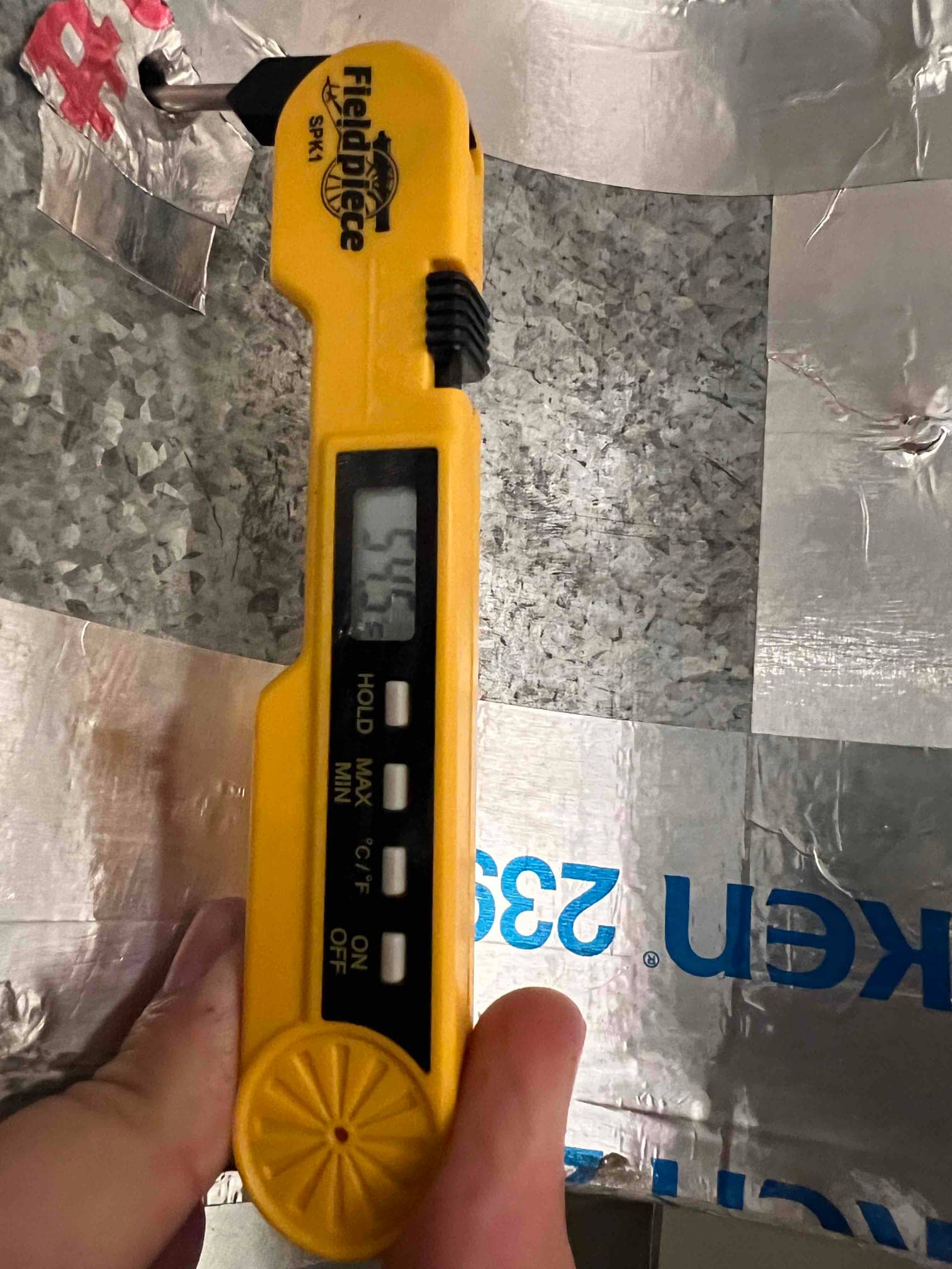 Digital thermometer probe inserted into ductwork shows 57.4°F, documenting supply air temperature leaving the evaporator.