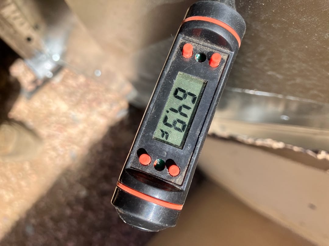 Digital thermometer probe measures air temperature in ductwork, displaying 66.9 degrees on the screen during commissioning checks.