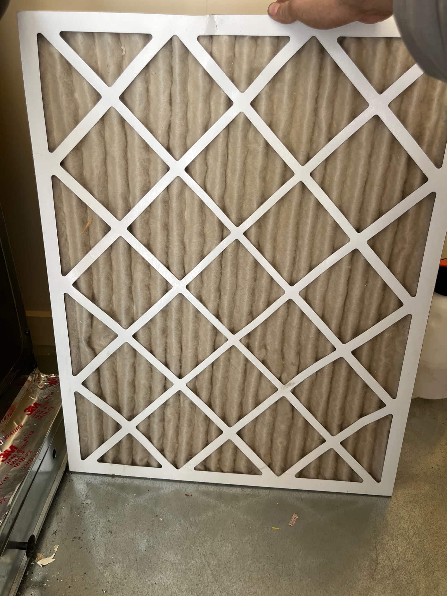 Dirty pleated air filter removed from the air handler, showing heavy dust accumulation across the filter media.