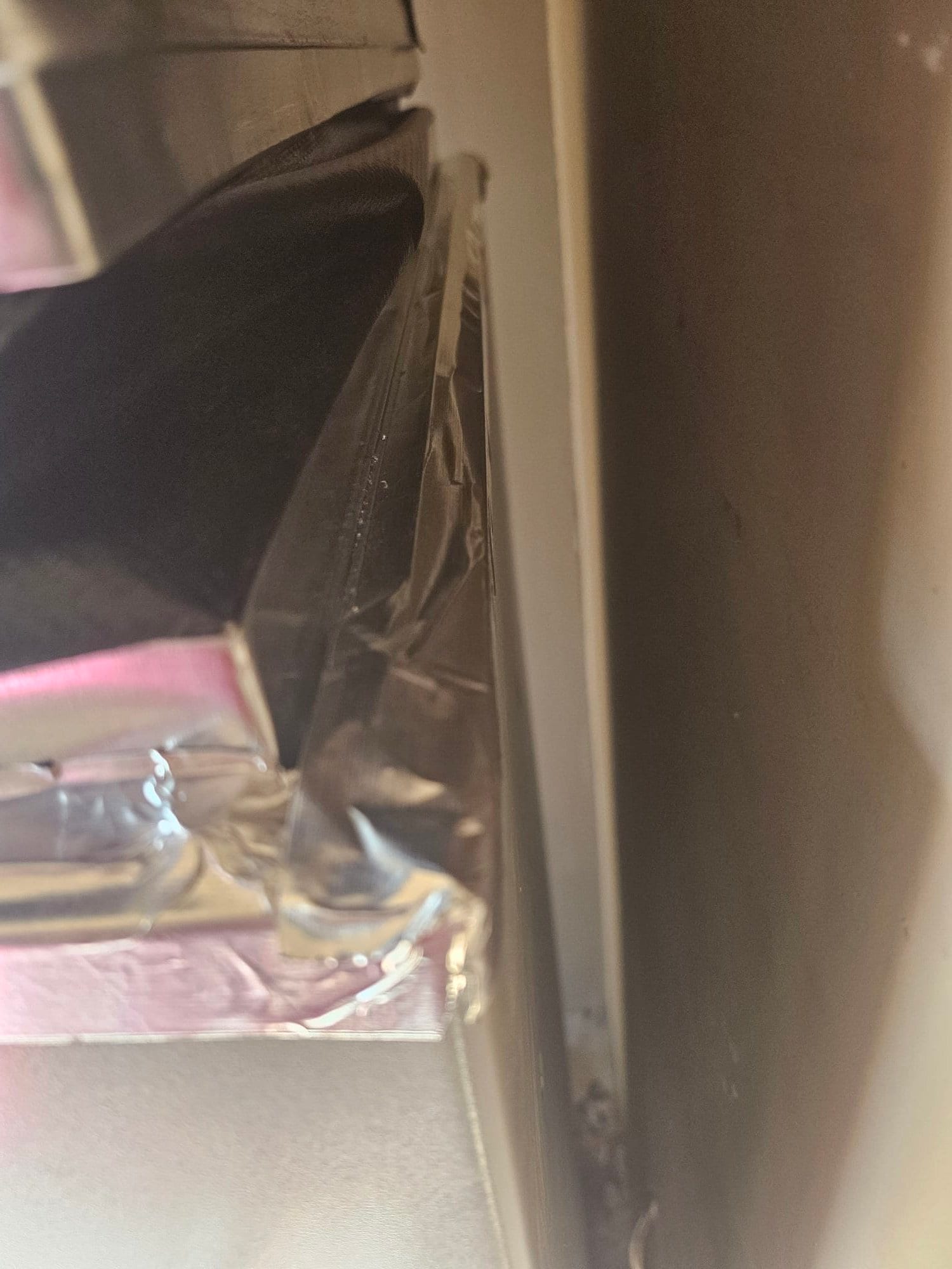 Foil tape seals the air handler cabinet joint against the adjacent wall, showing tight clearances and finished duct connection.