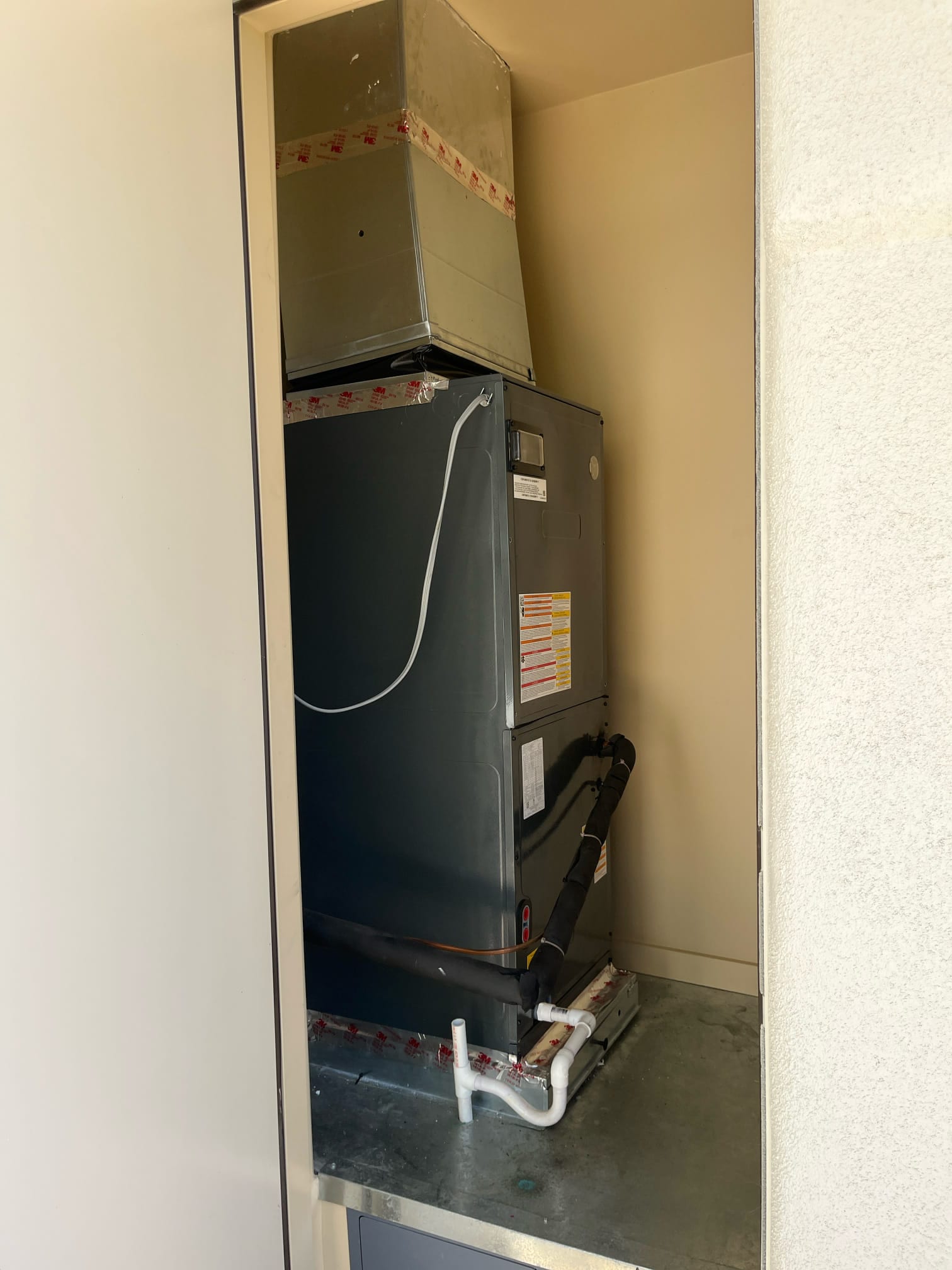 Indoor air handler in a closet with insulated refrigerant lines and PVC condensate drain piping visible at the base.