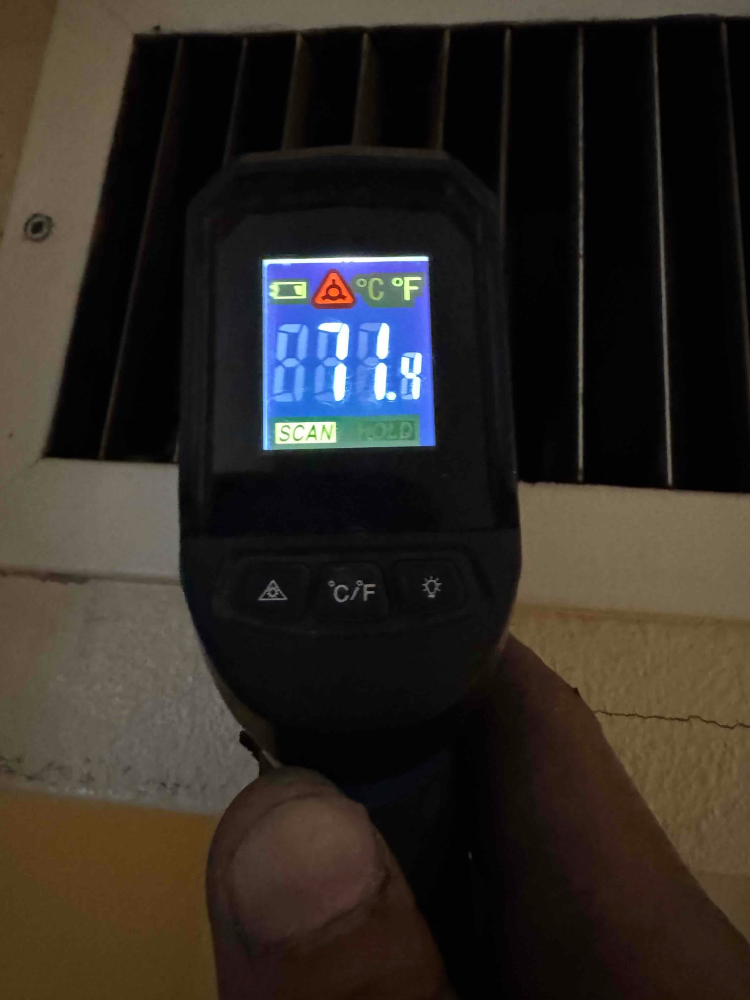 Infrared thermometer aimed at a return grille shows 87.4 degrees Fahrenheit during air-side commissioning.