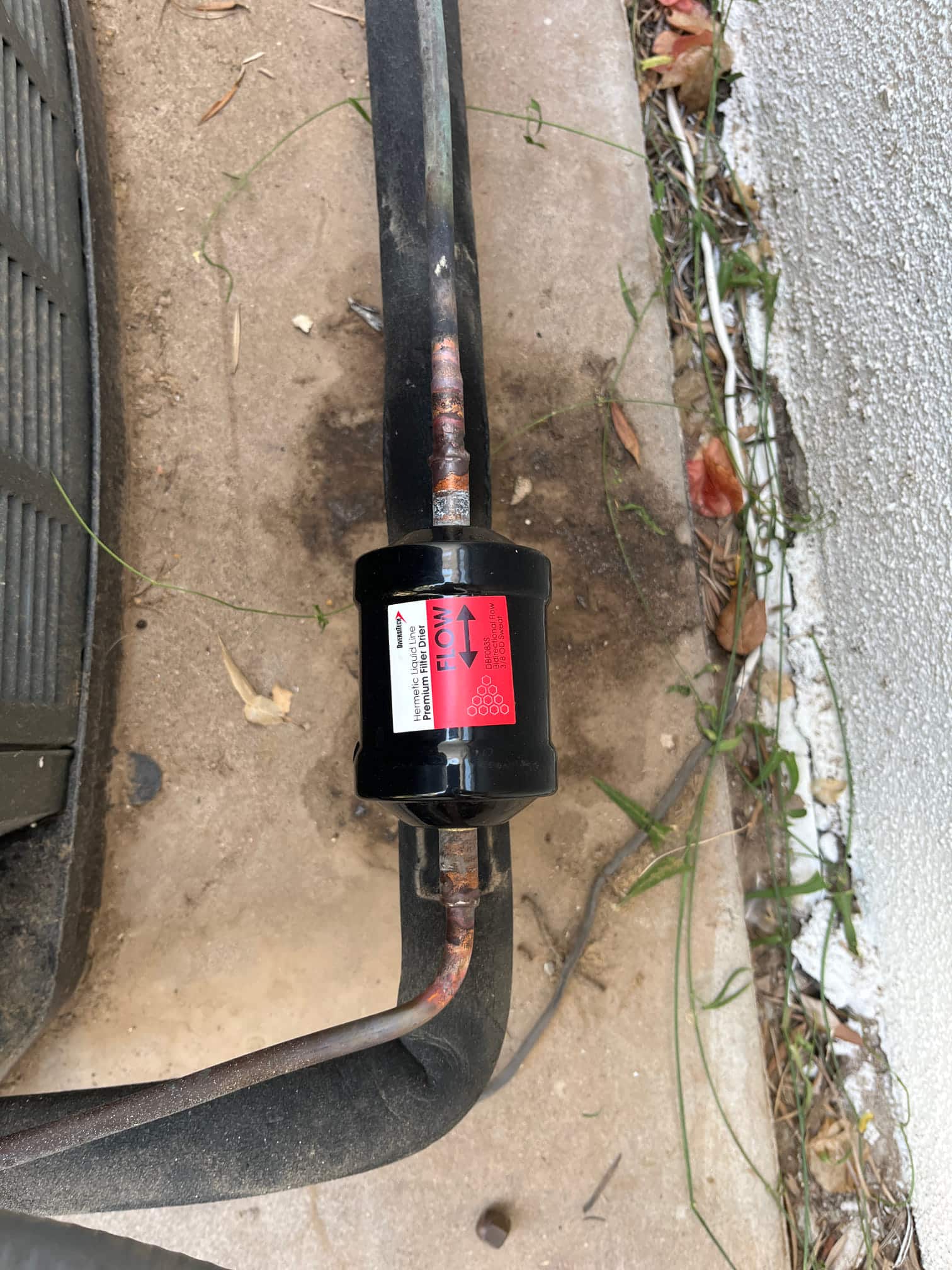 Inline refrigerant filter-drier installed on the suction line, showing clean brazed joints and insulated tubing near the condenser.