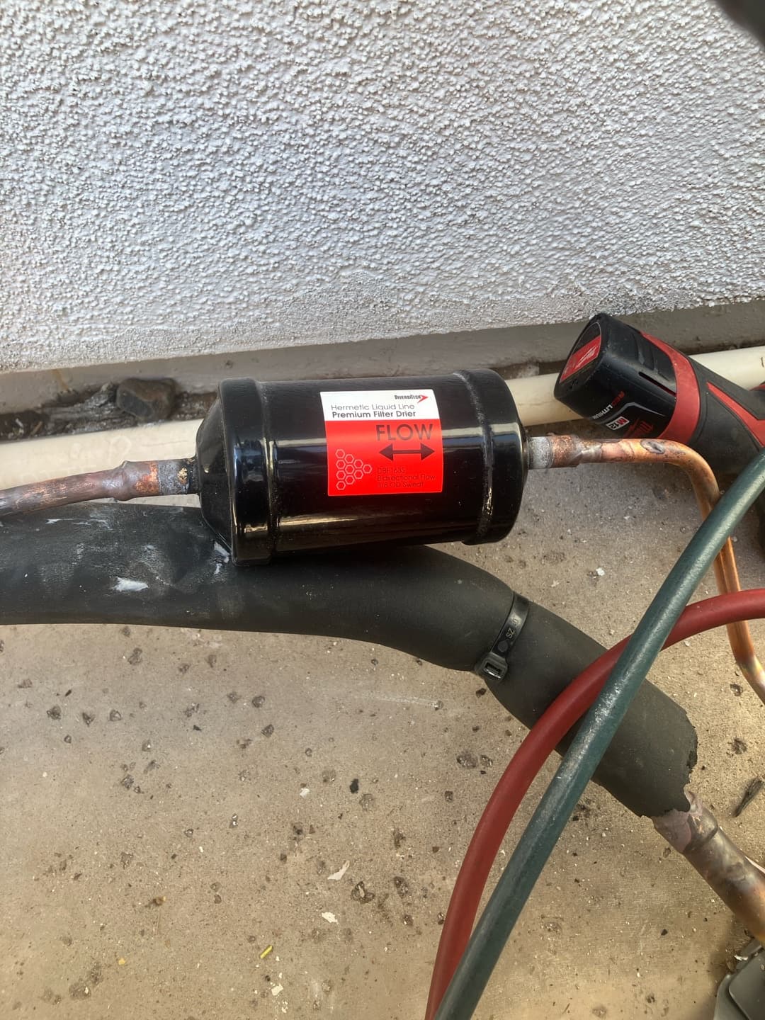 Liquid-line filter drier brazed into the refrigerant line set with correct flow direction indicated by the arrow label.