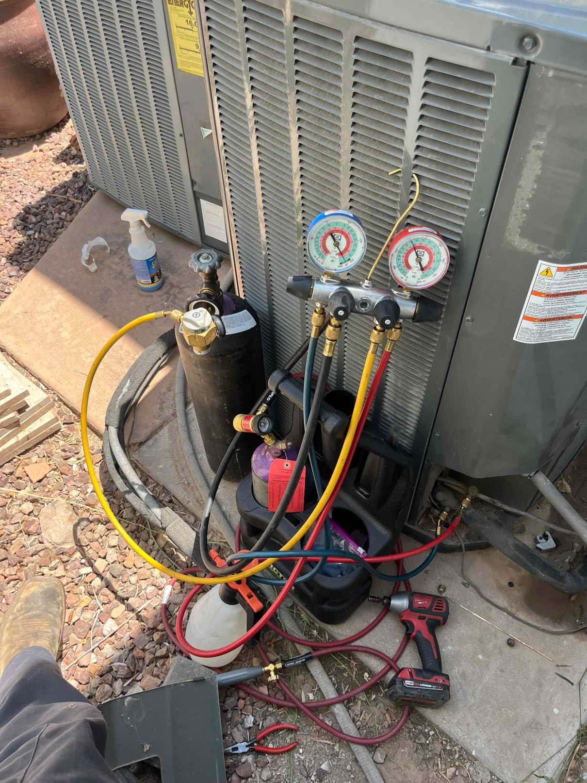 Manifold gauges connected to the outdoor condenser during service, with refrigerant cylinders and hoses arranged for charging or recovery.