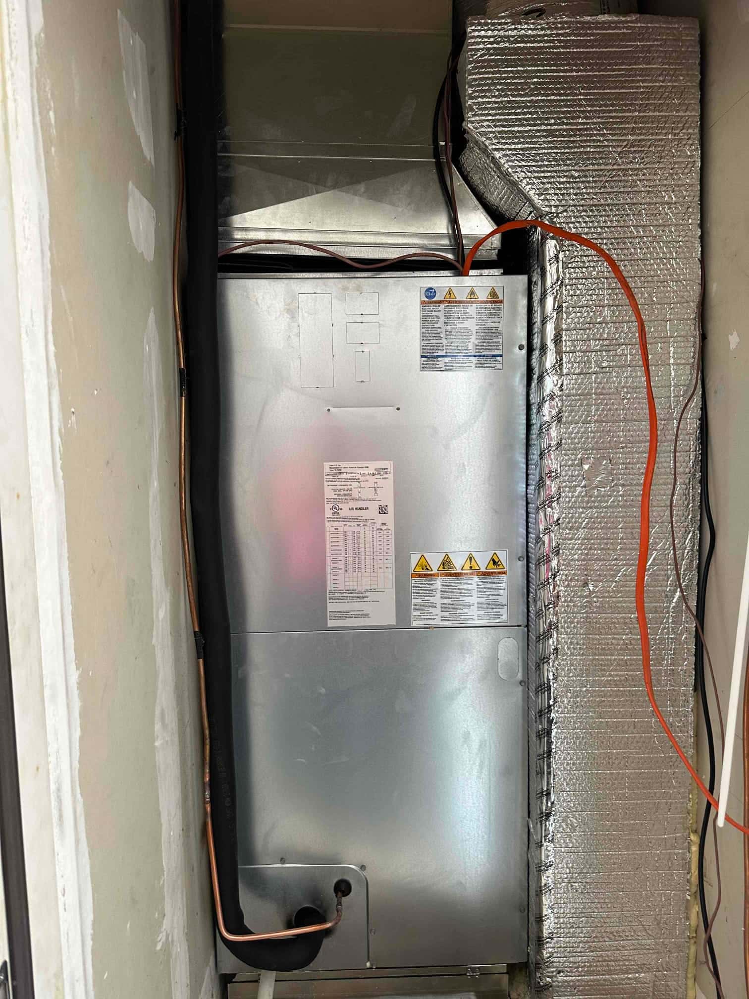 New air handler installed in a closet with insulated suction line, sealed duct connections, and drain line routing at the base.