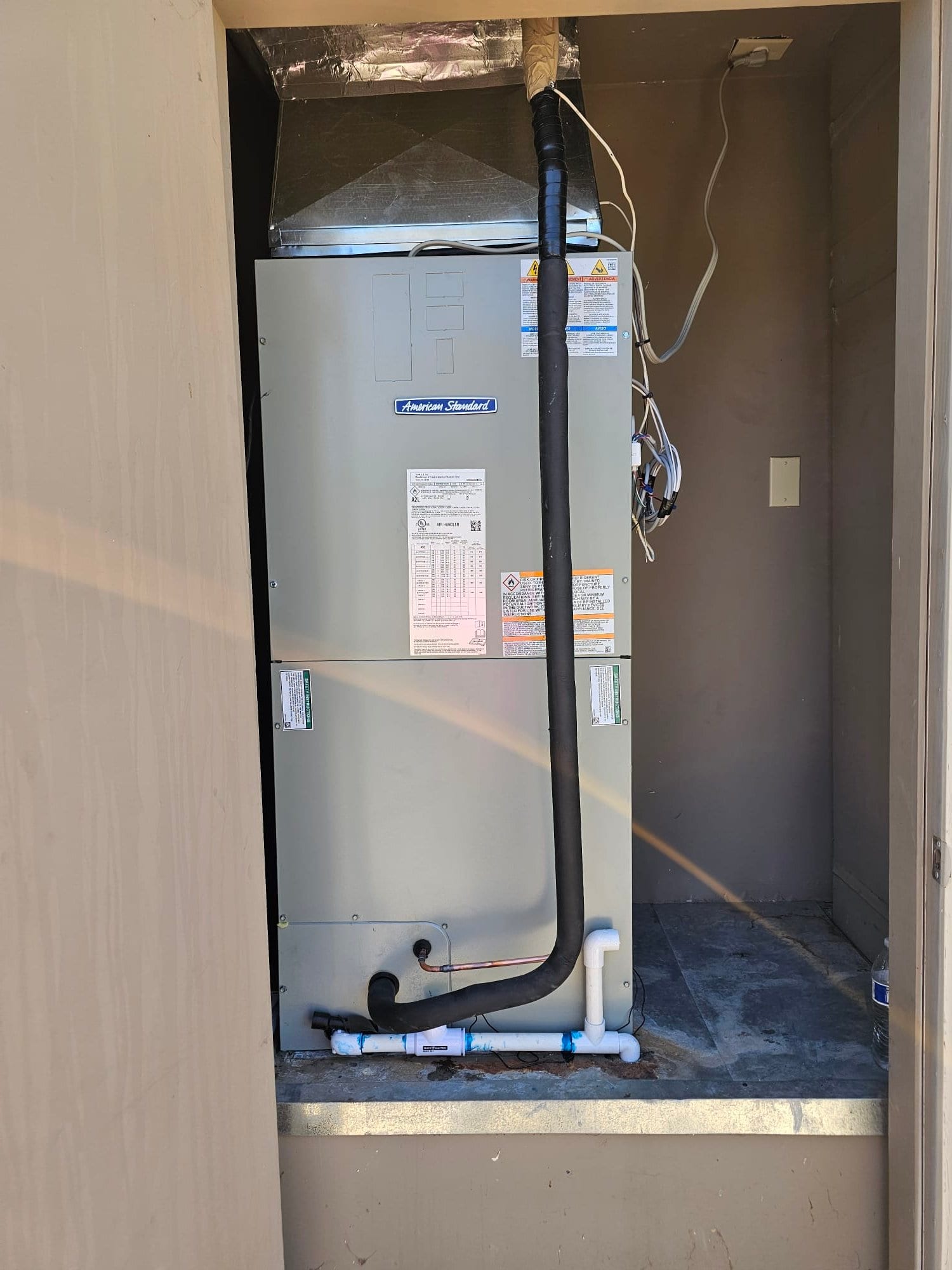 New air handler set in closet with insulated refrigerant lines, sealed duct transitions, and PVC condensate drain assembly installed.