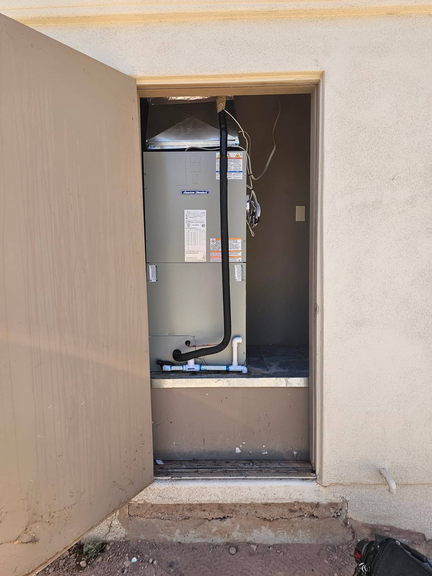 New air handler set in a utility closet with insulated refrigerant line and newly plumbed condensate drain piping.