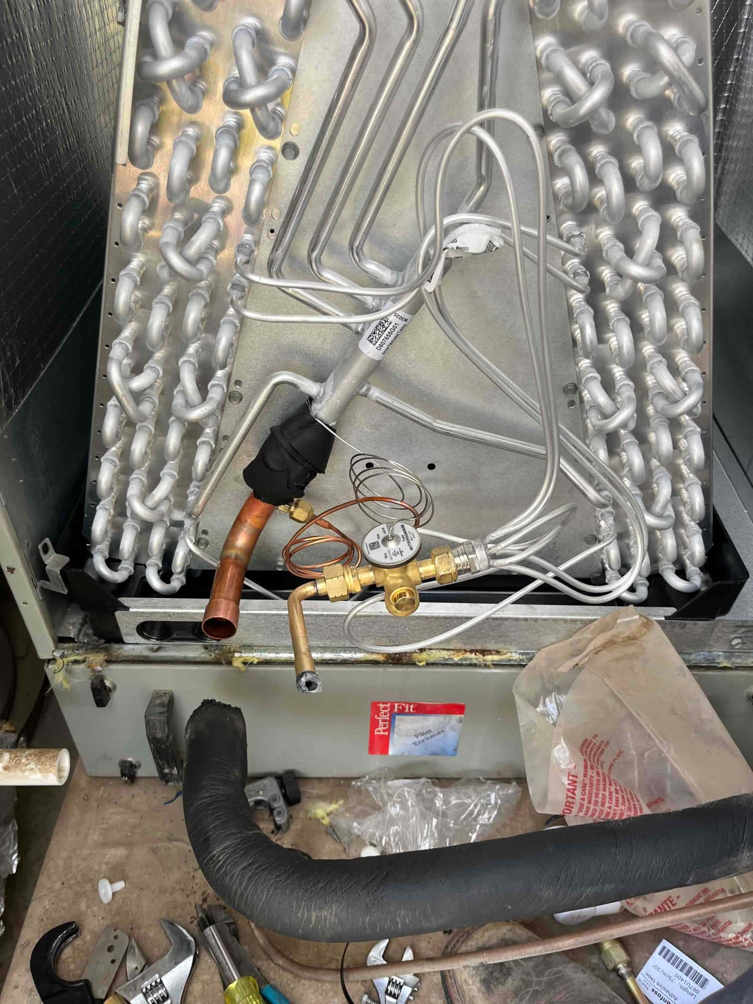 New evaporator coil installed with thermal expansion valve and sensing bulb secured, refrigerant lines positioned for connection inside the air handler.