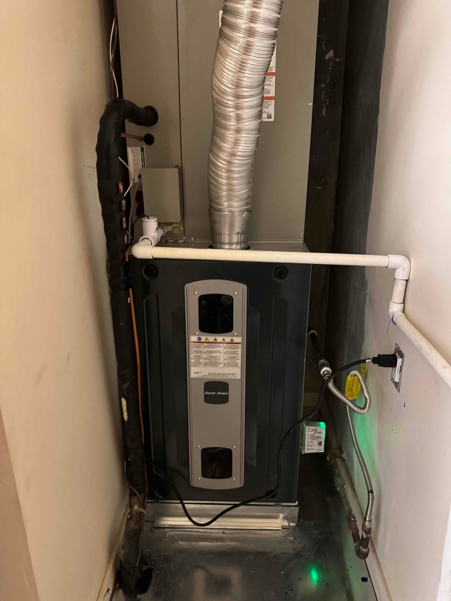 New gas furnace installed with insulated refrigerant lines, condensate drain piping, flexible gas connector, and vent piping, set on a drain pan.