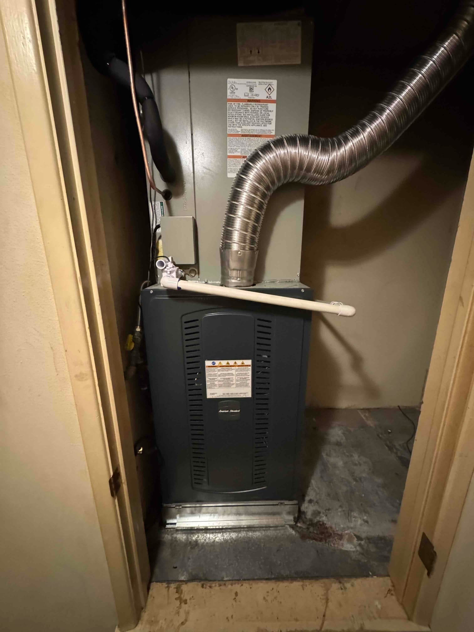 New indoor furnace and coil assembly installed in a closet, with flexible metal flue, insulated refrigerant line, and condensate drain.