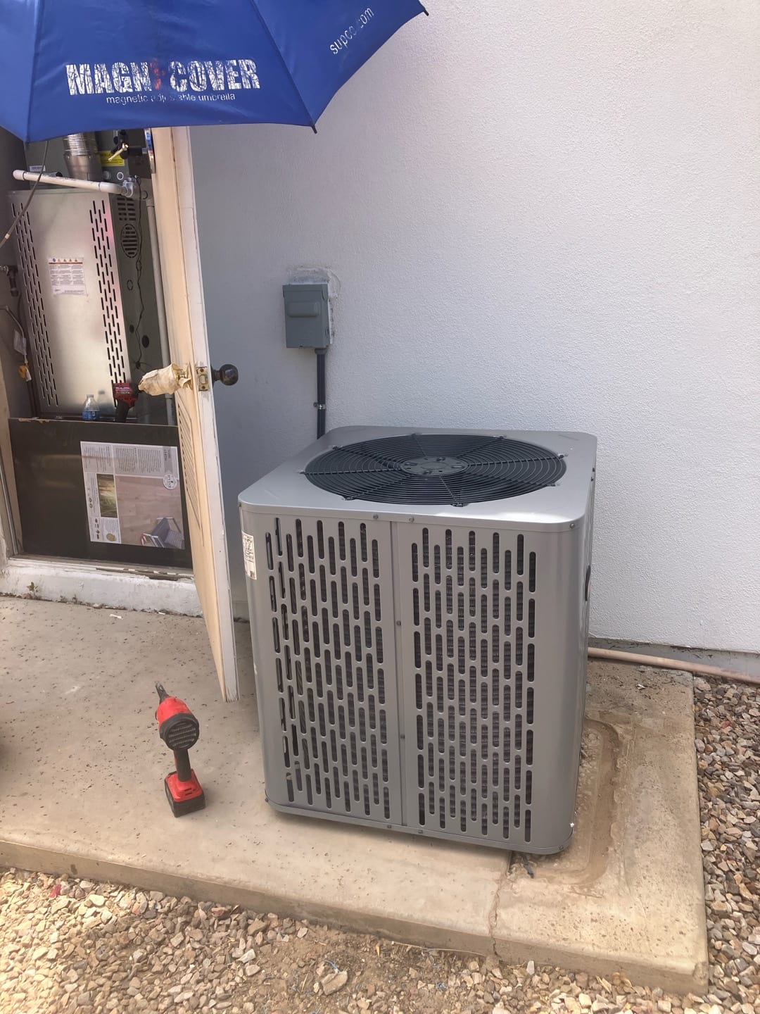 New outdoor condenser set on a concrete pad beside the service disconnect, with indoor furnace cabinet open during installation.