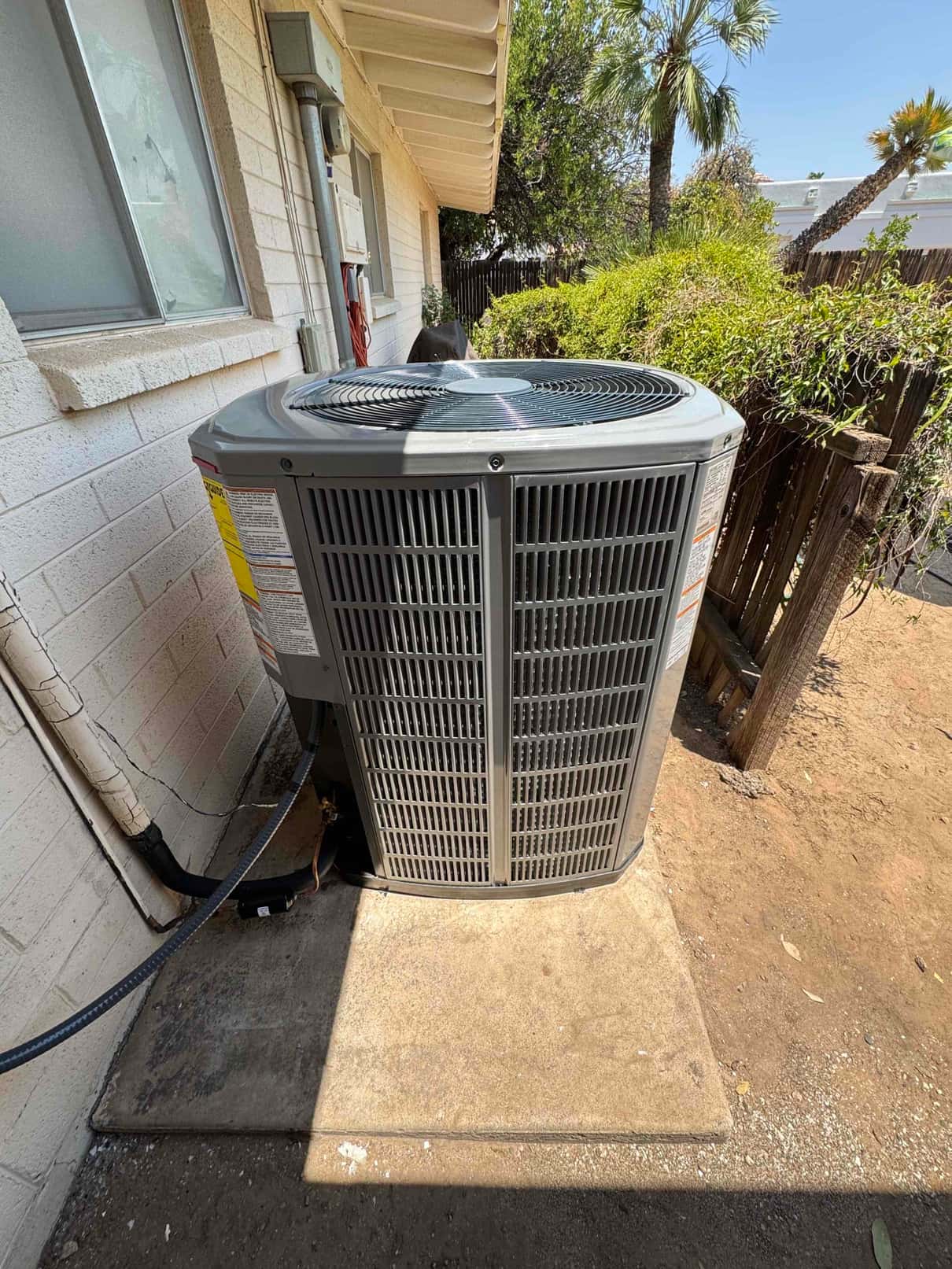 New outdoor condenser set on a concrete pad with insulated line set and electrical whip connected along the wall.