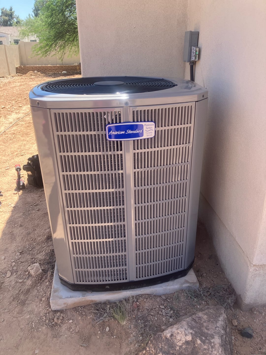 New outdoor condenser set on a level pad with nearby electrical disconnect mounted on the wall and line set routed.