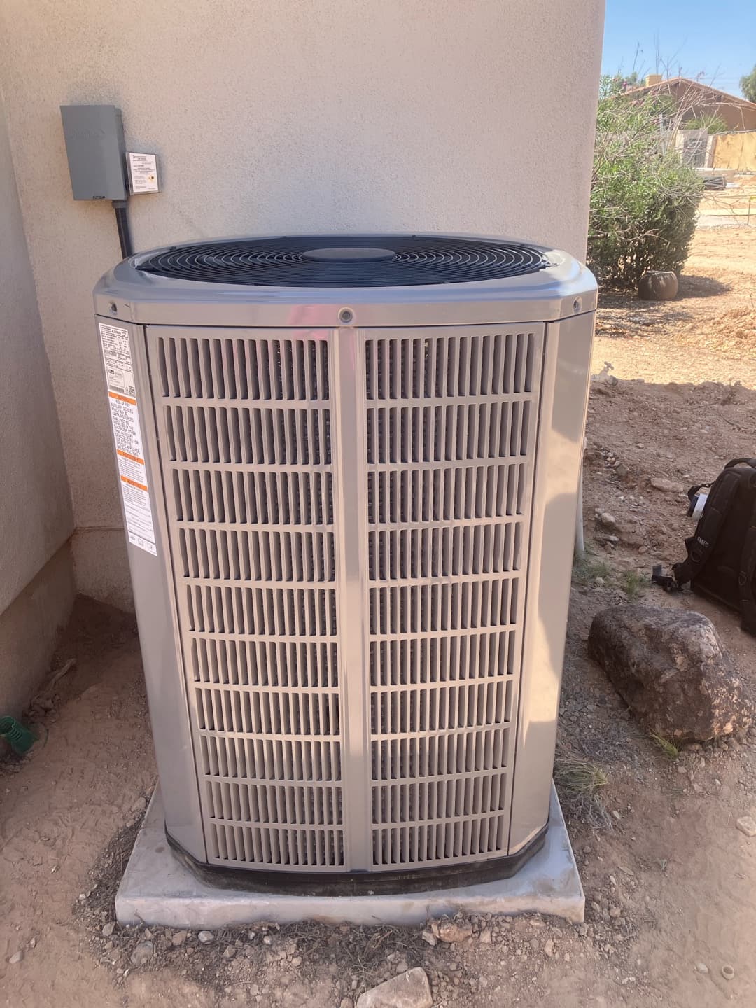 New outdoor condenser set on a level pad with weatherproof disconnect mounted on the wall and sealed line penetration.
