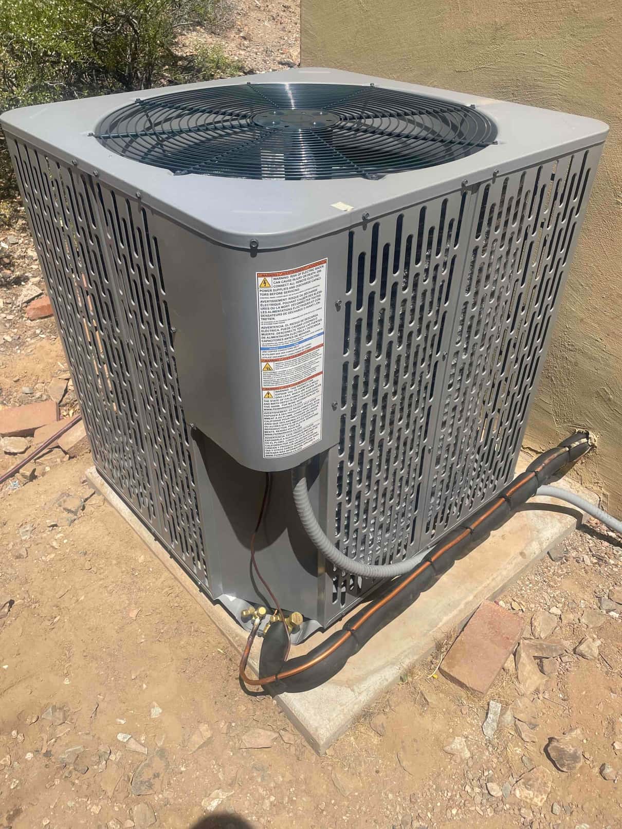 New outdoor heat pump condenser set on a level pad with insulated refrigerant lines and electrical whip connected.