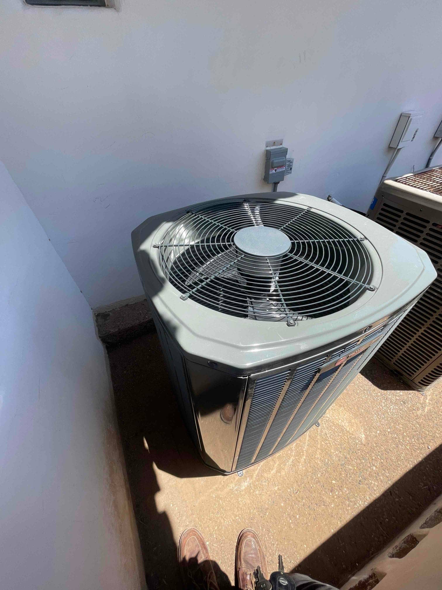 New outdoor heat pump condenser set on a level pad with nearby electrical disconnect mounted on the wall.