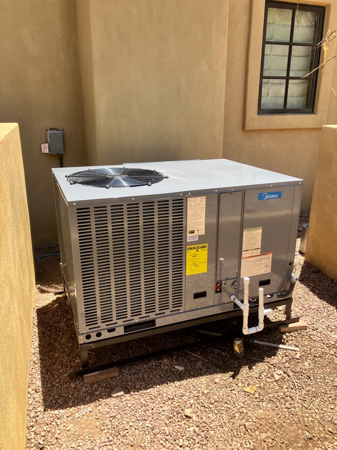 New packaged HVAC unit set outdoors on a metal frame with condensate drain piping and electrical disconnect nearby.