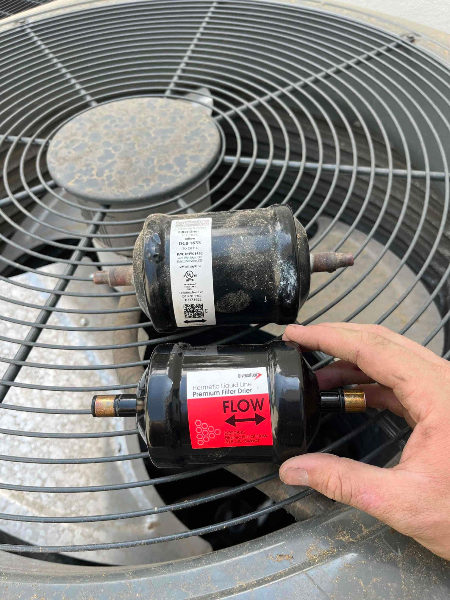 Old refrigerant line filter-drier removed and new premium filter-drier with flow direction arrow ready for installation.