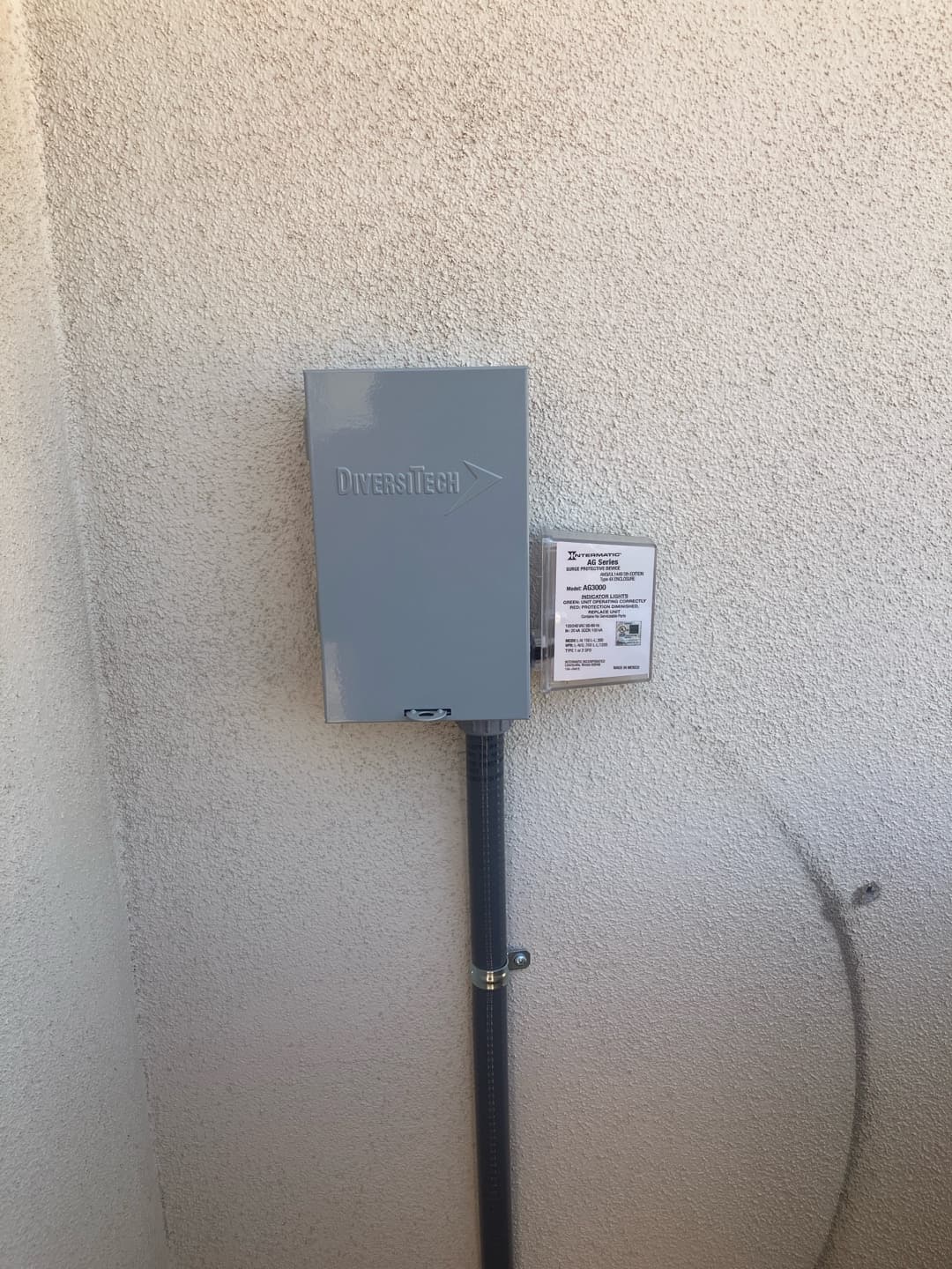 Outdoor AC disconnect box with flexible conduit neatly secured to the wall beside a surge protective device.