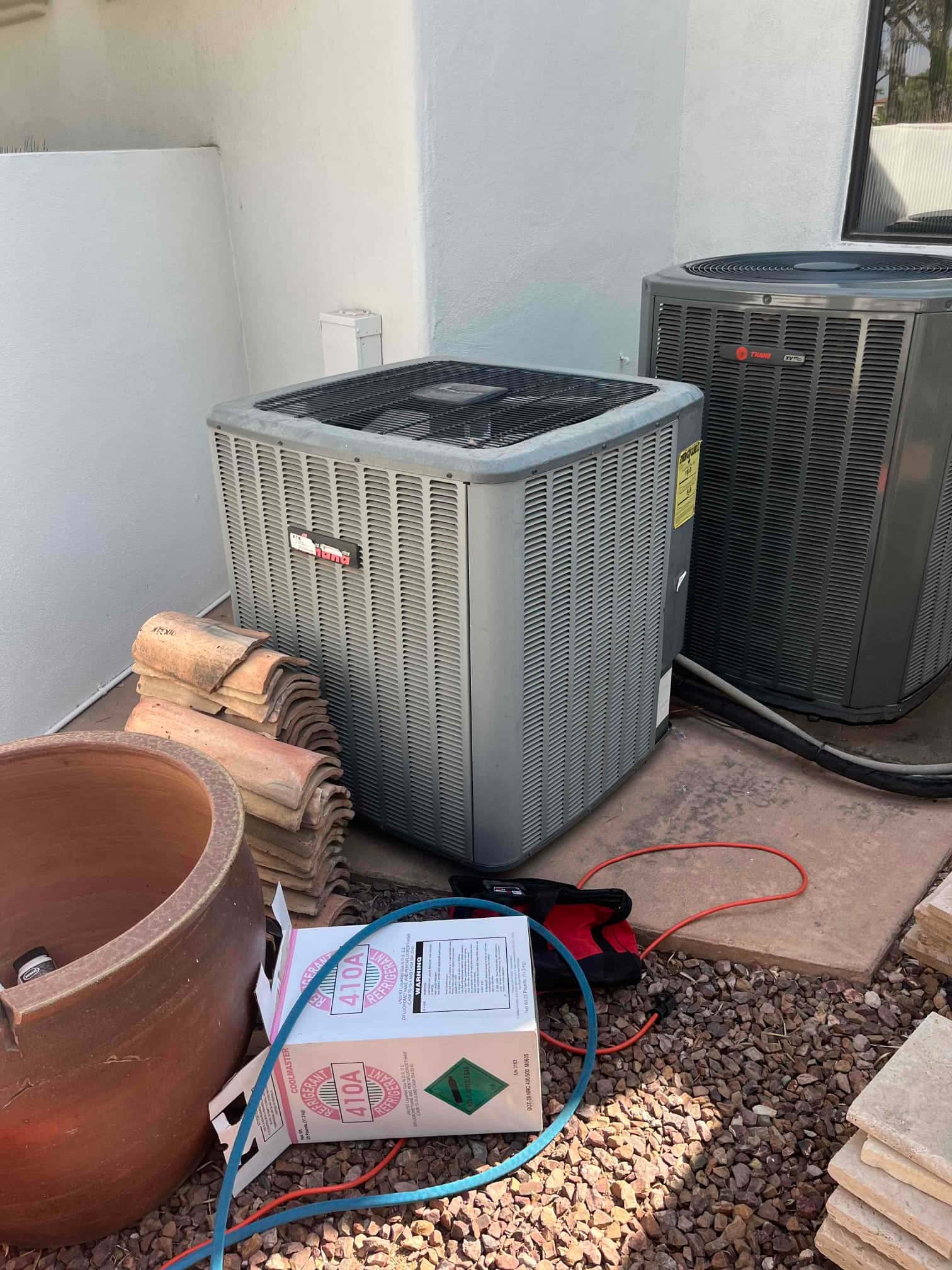 Outdoor air conditioning condensing units with service hoses and tools on the ground during repair work.