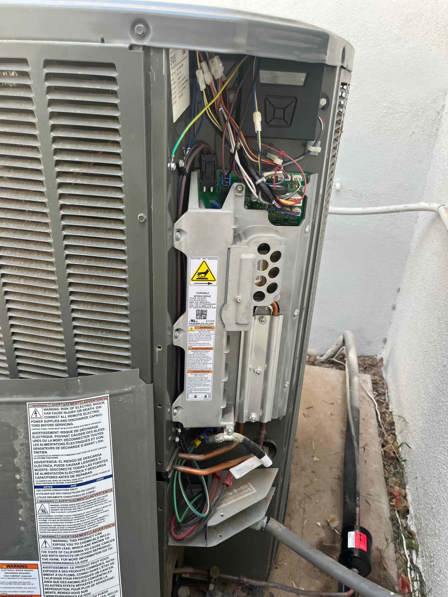 Outdoor condenser cabinet open, exposing control board, contactor, wiring harnesses, and service valves with refrigerant lines routed to the unit.
