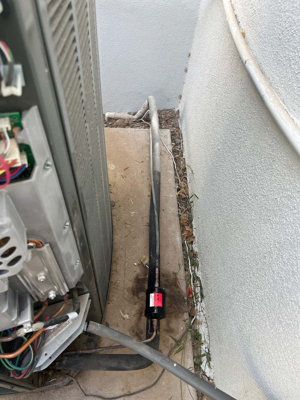 Outdoor condenser with open electrical panel and insulated refrigerant line set on the pad beside the unit.