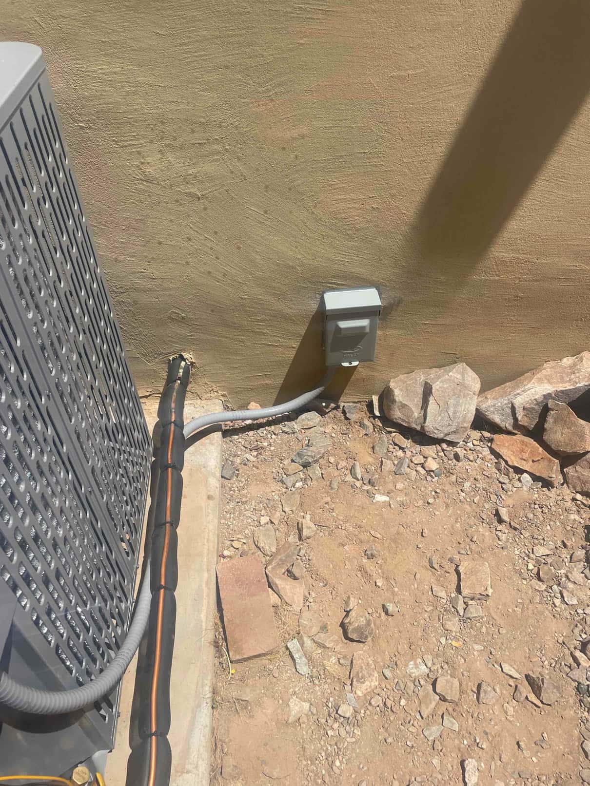 Outdoor condenser set on a pad with insulated line set and weatherproof electrical disconnect mounted on the wall.