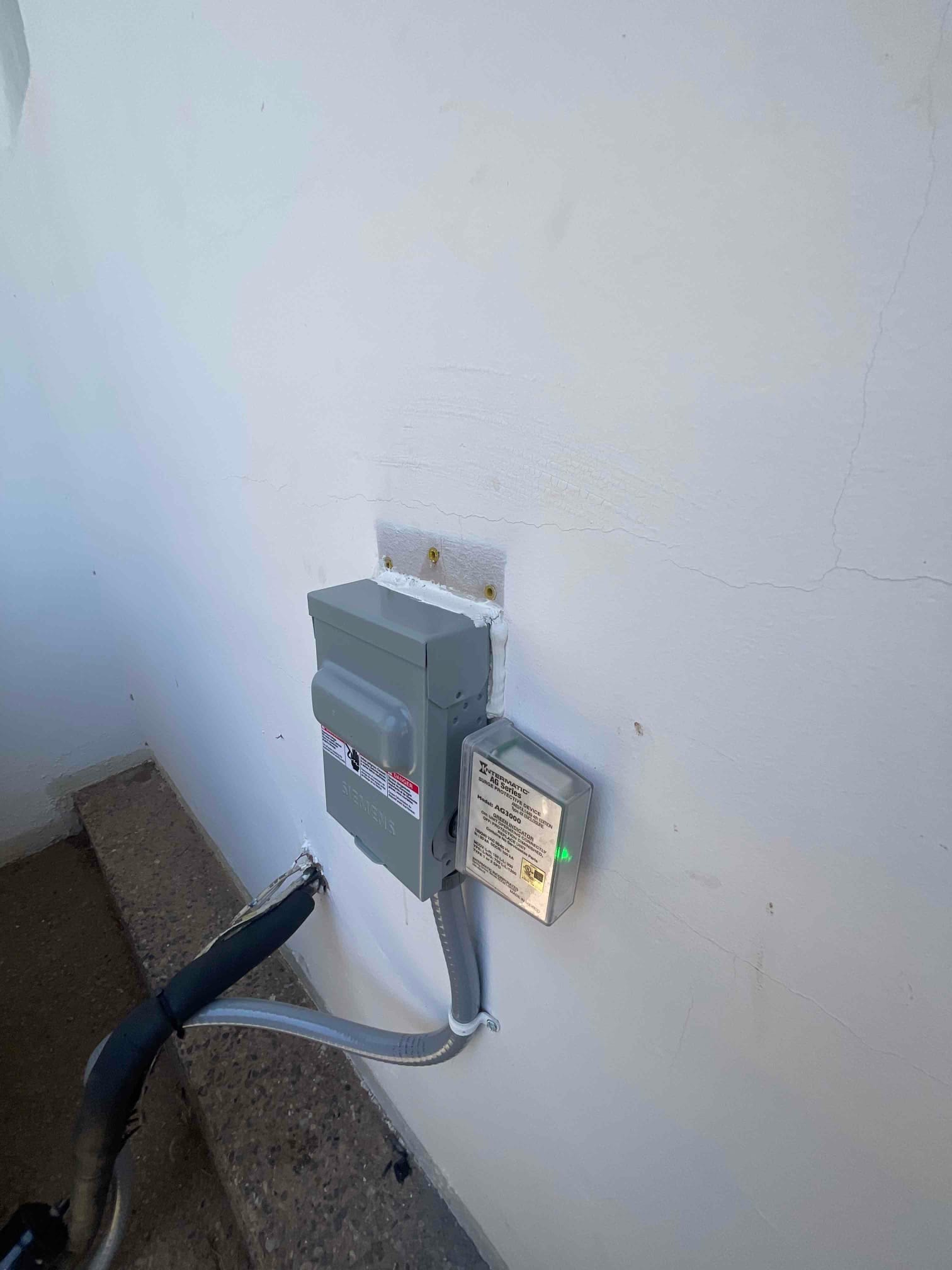 Outdoor disconnect with flexible conduit and surge protective device mounted beside it, neatly sealed to the exterior wall.