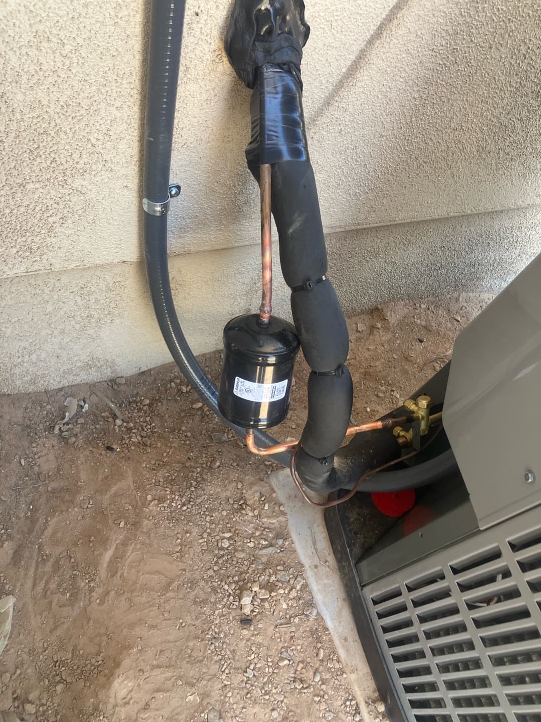 Refrigerant line set with insulation, filter drier, and sealed wall penetration connected to the new outdoor condenser.