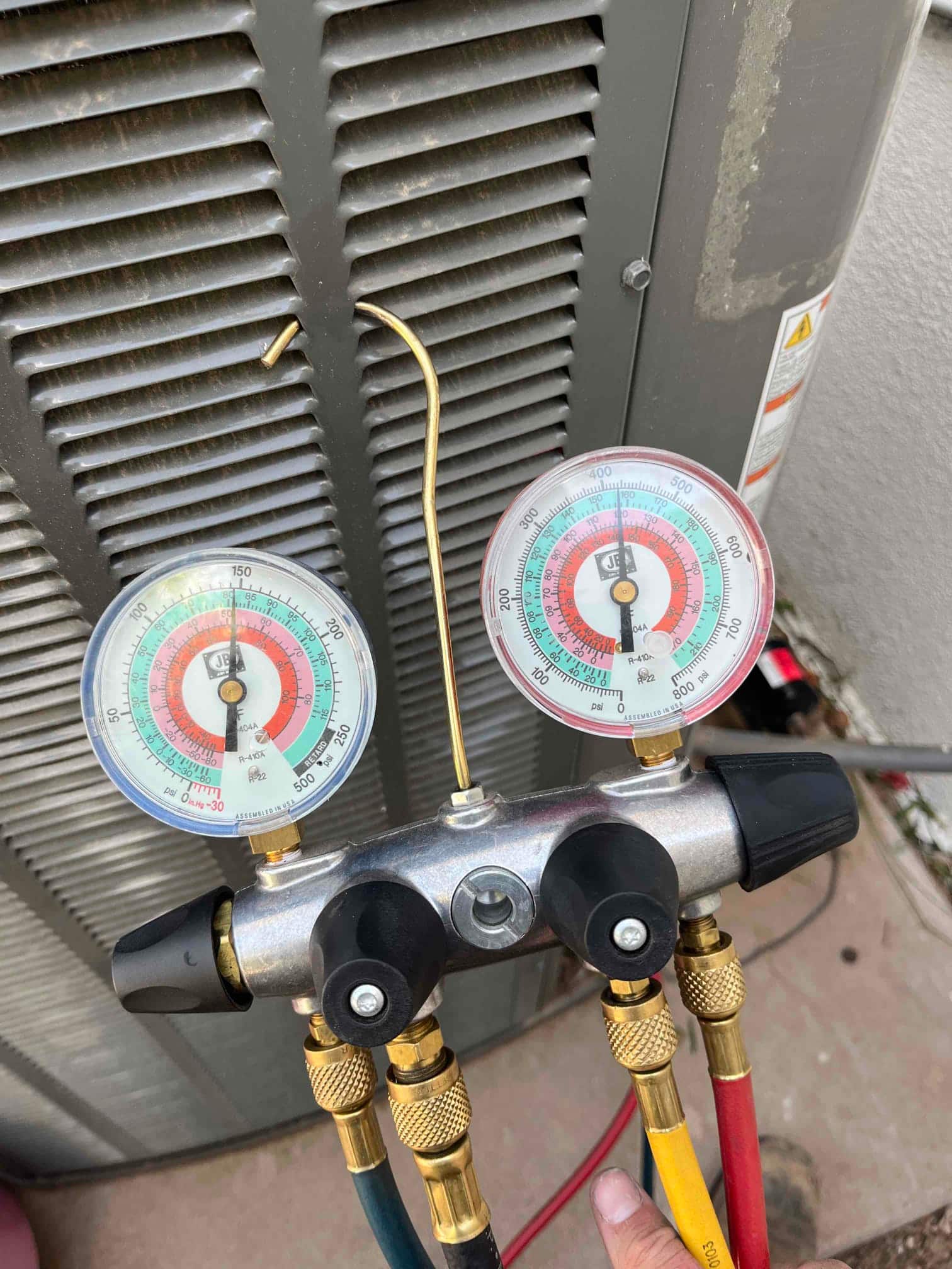 Refrigerant manifold gauges connected at the outdoor unit during service, showing low-side and high-side pressures for system diagnostics.