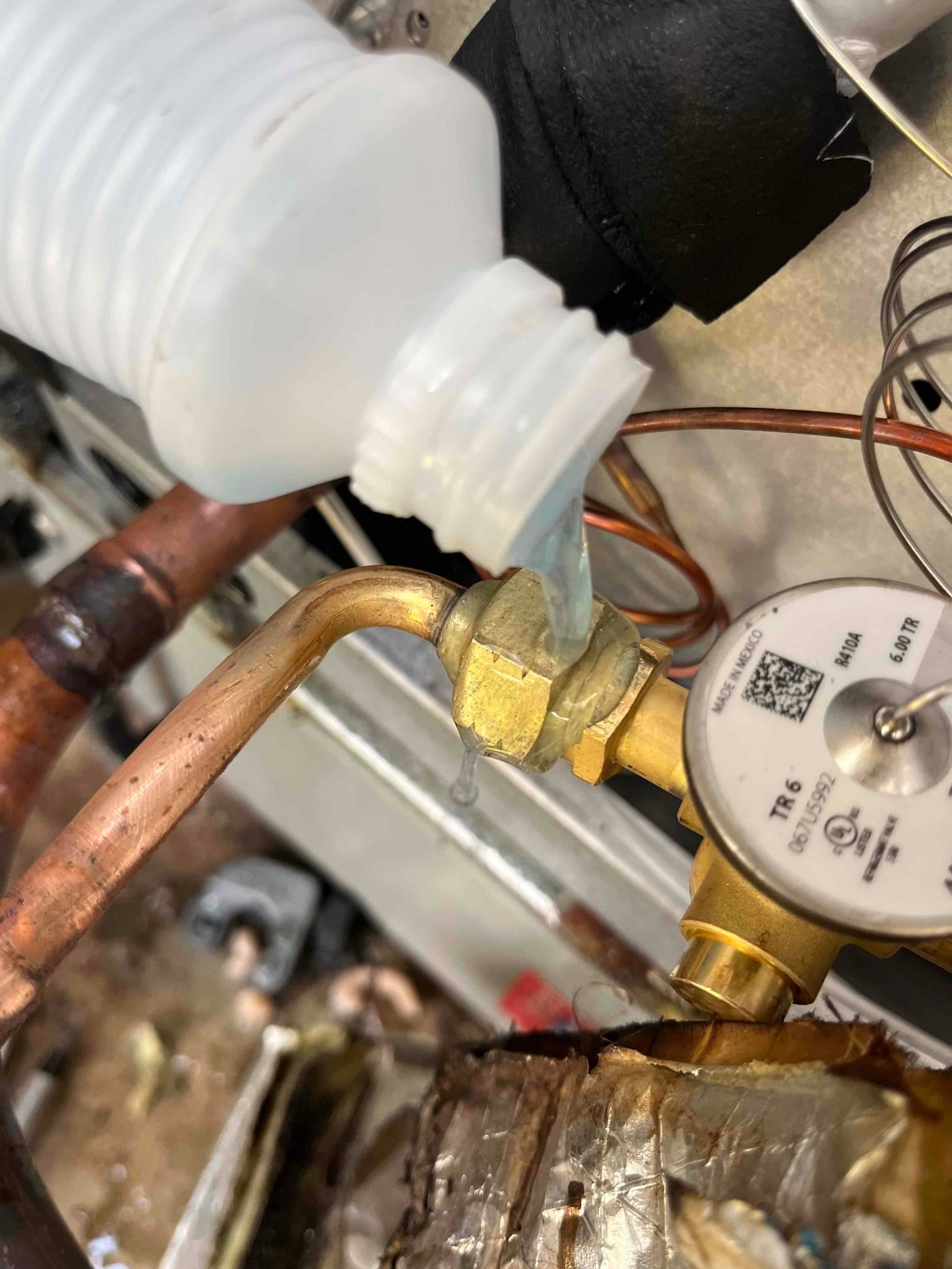 Technician applies leak detection solution to a brass service valve while gauge manifold is connected to the refrigeration line.