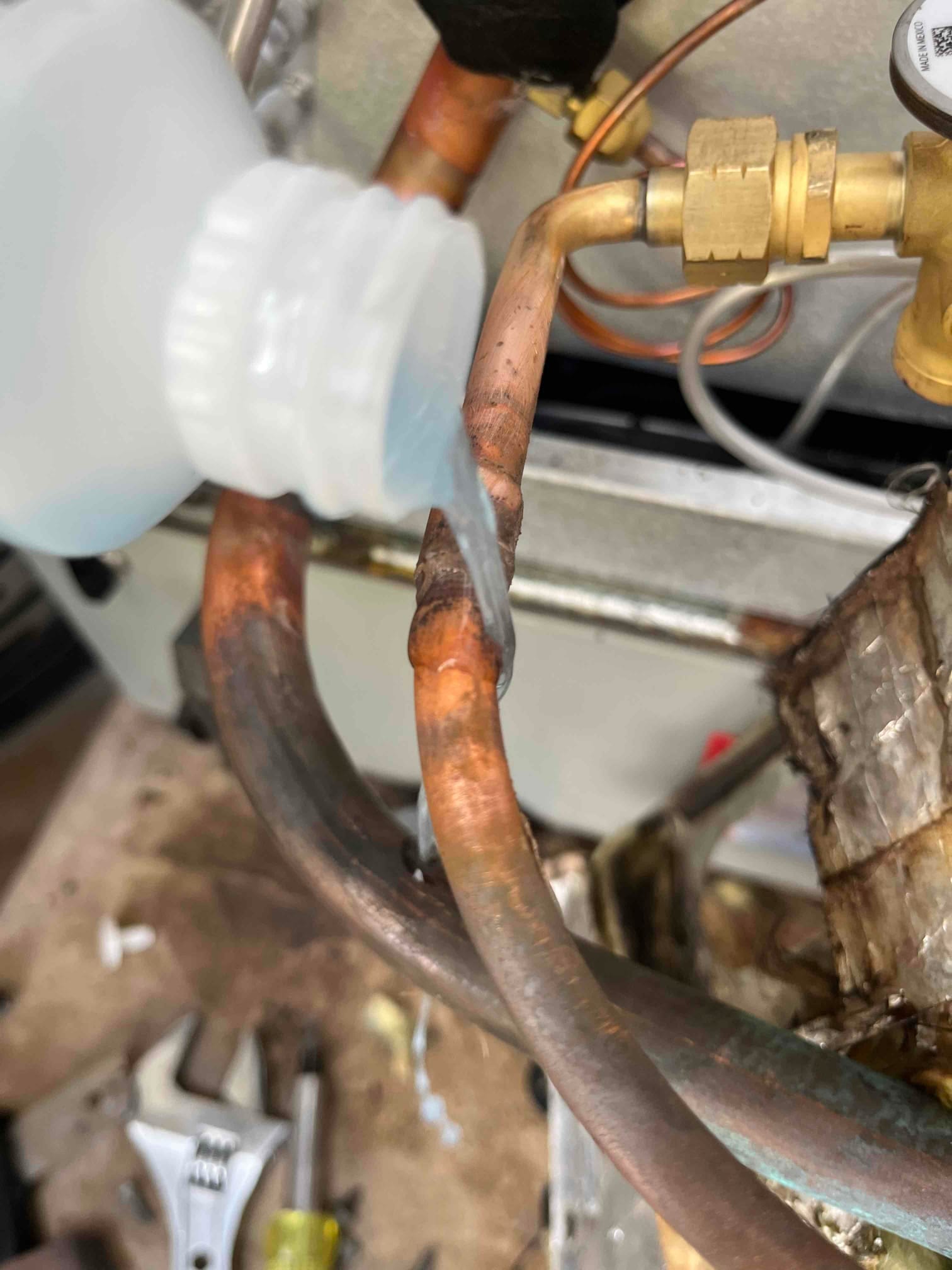 Technician applies leak detection solution to a brazed copper refrigerant line joint near a service valve and coil.